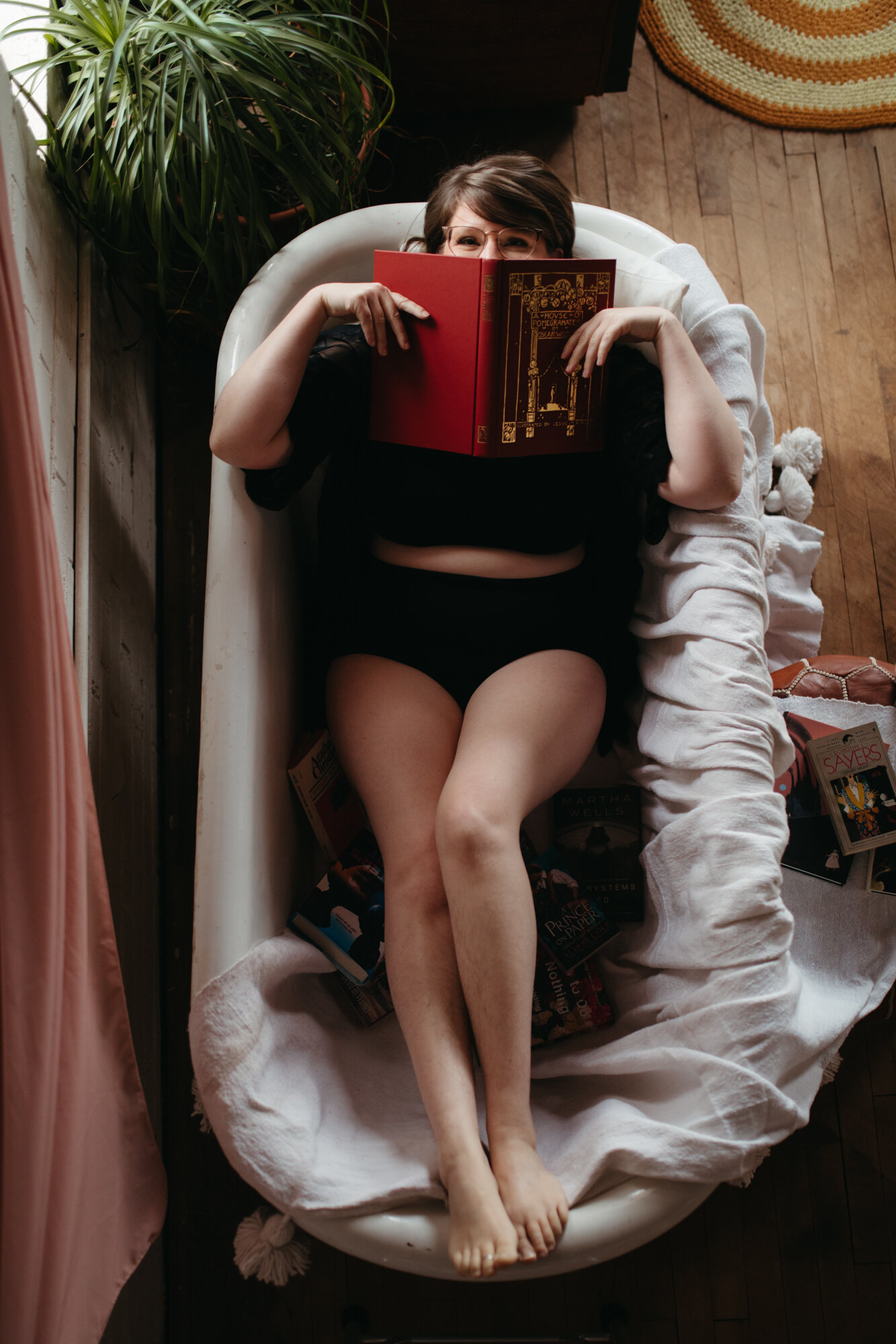 Fun boudoir portrait of person in bathtub holding book over bottom half of face