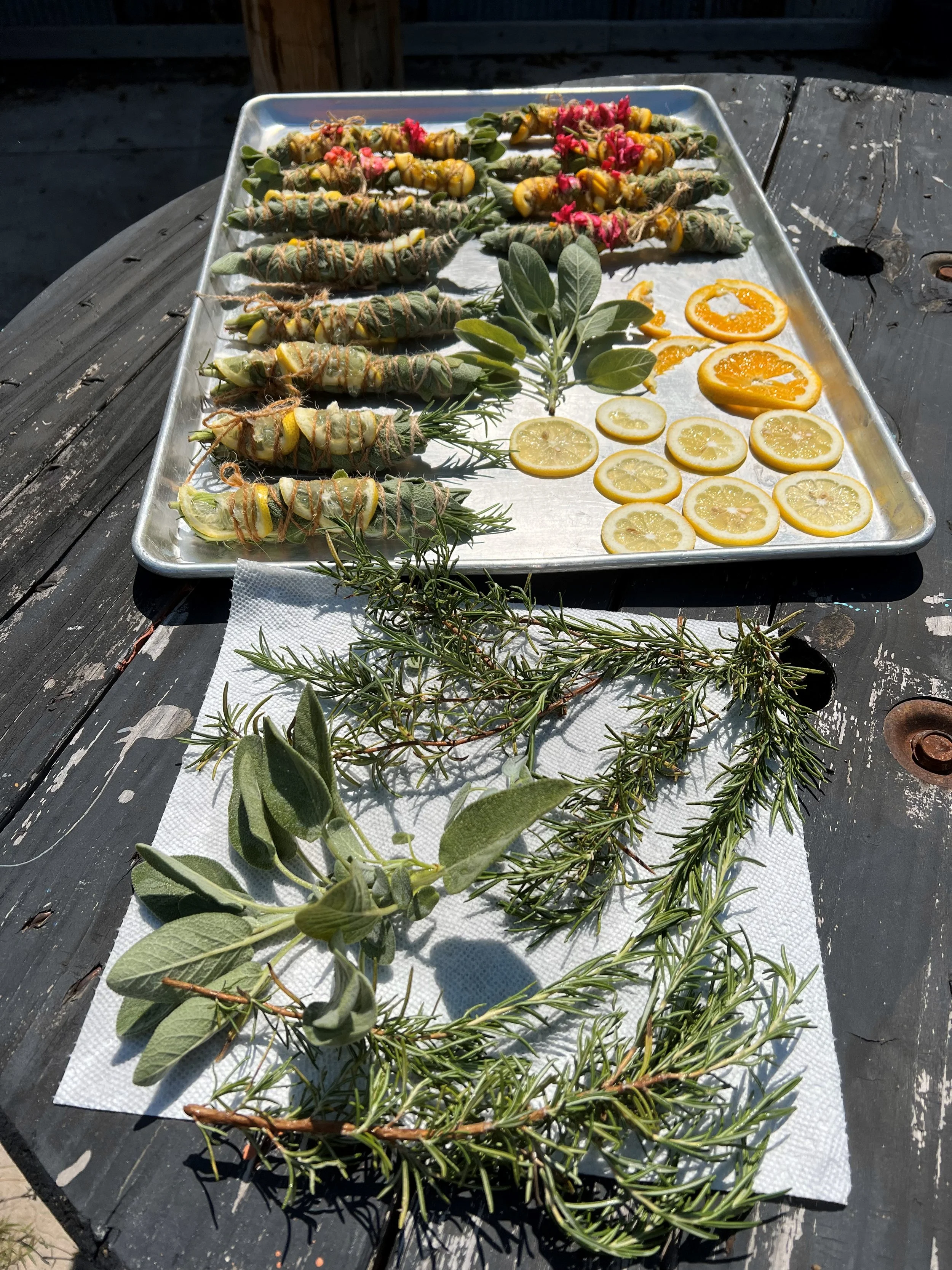 Herbs, lemon slices, and herbs tied with string on a silver tray outside on a wooden table.