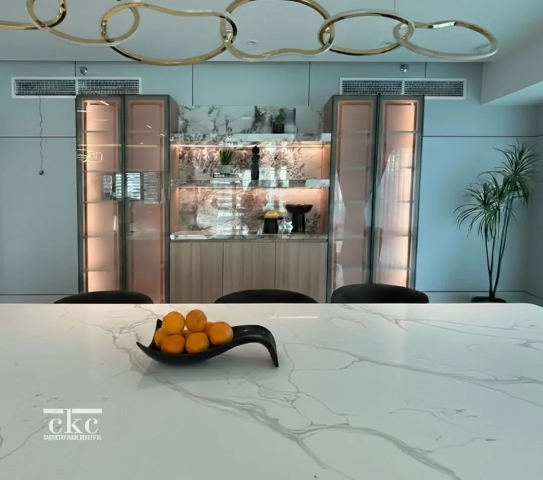 The perfect balance does exist. ✨ This custom display unit is a masterclass in texture, blending warm wood tones, sleek illuminated glass cabinetry, and a stunning stone-finish backsplash that perfectly mirrors the island. It&rsquo;s not just storage