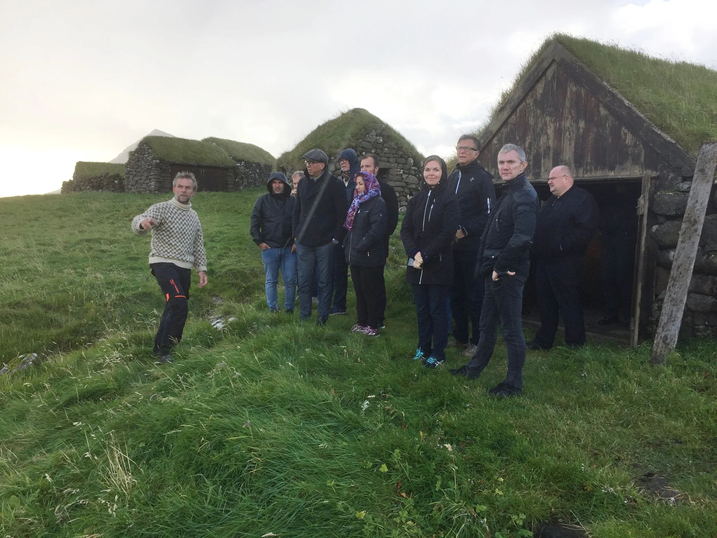 Á myndini standa gestirnir uttan fyri neystið har koltursbáturin stendur, meðan Bjørn greiðir frá atkomuviðurskiftunum í Koltri í gomlum døgum.