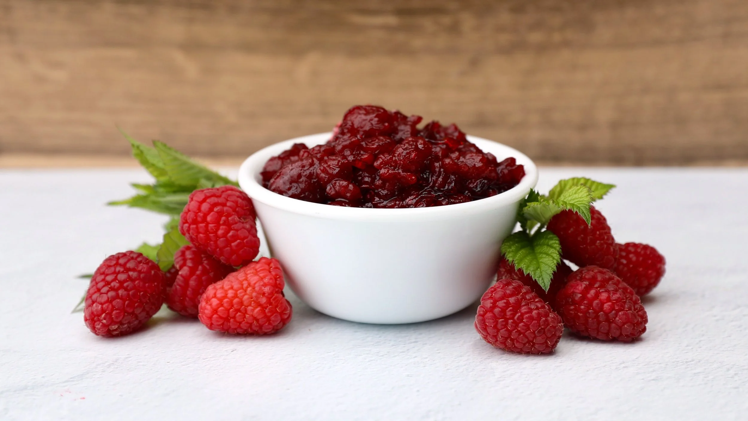 Raspberry topping in white bowl surrounded by fresh raspberries