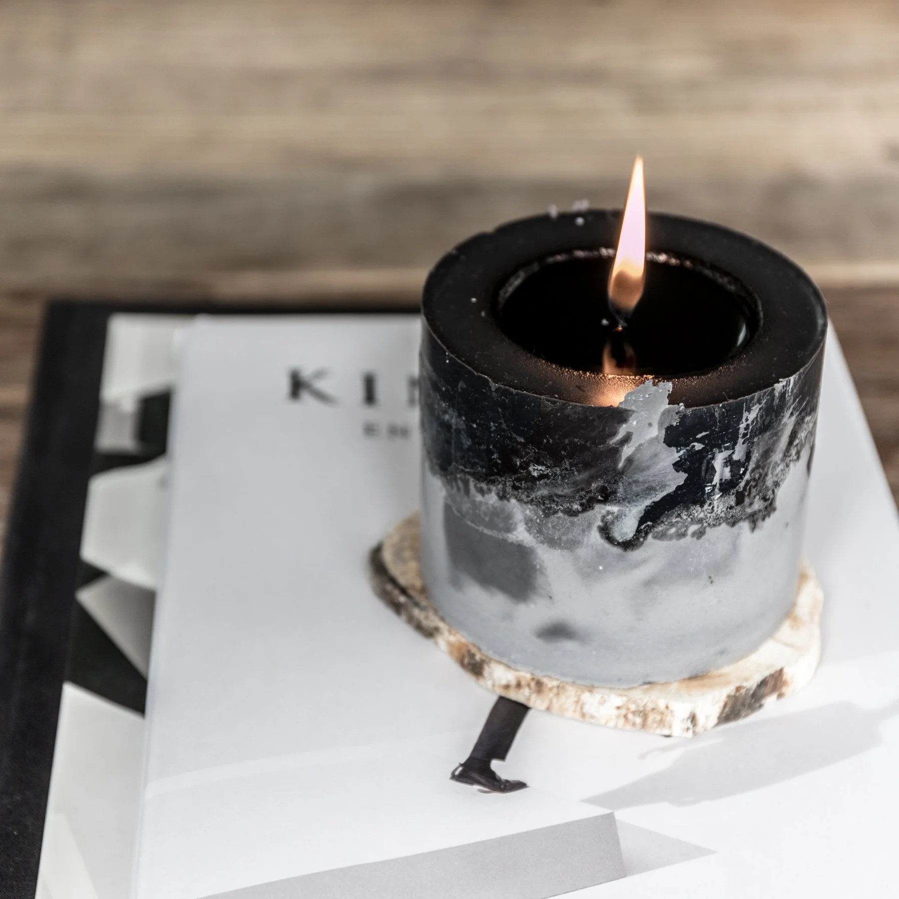 Black candle with flame on a white book cover on a wooden surface.