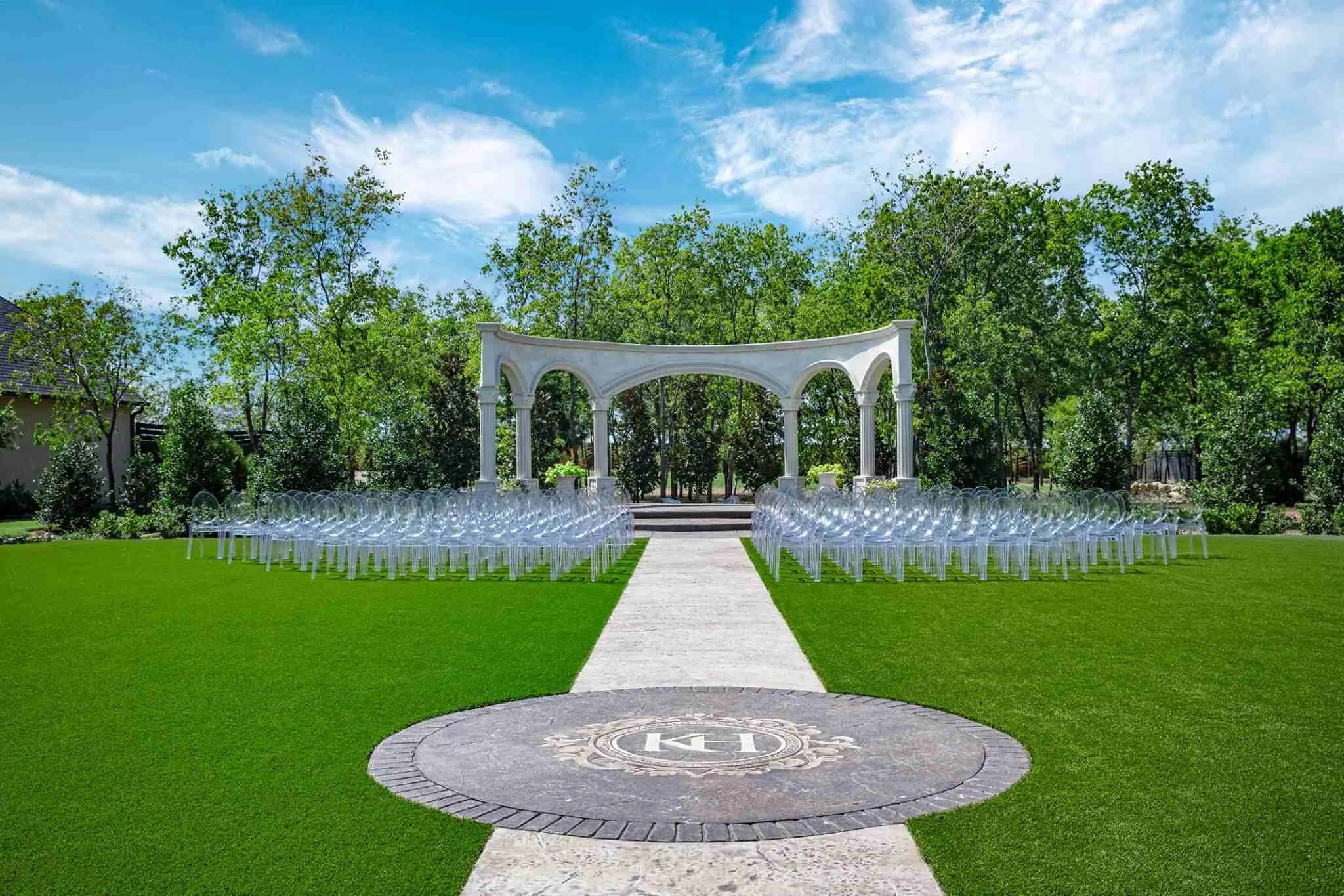 Outdoor wedding ceremony setup at Knotting Hill Place event lawn featuring 300-guest  seating, white ceremony chairs, elegant arch, professional staging, and lush green  synthetic grass for Dallas-Fort Worth ceremonies