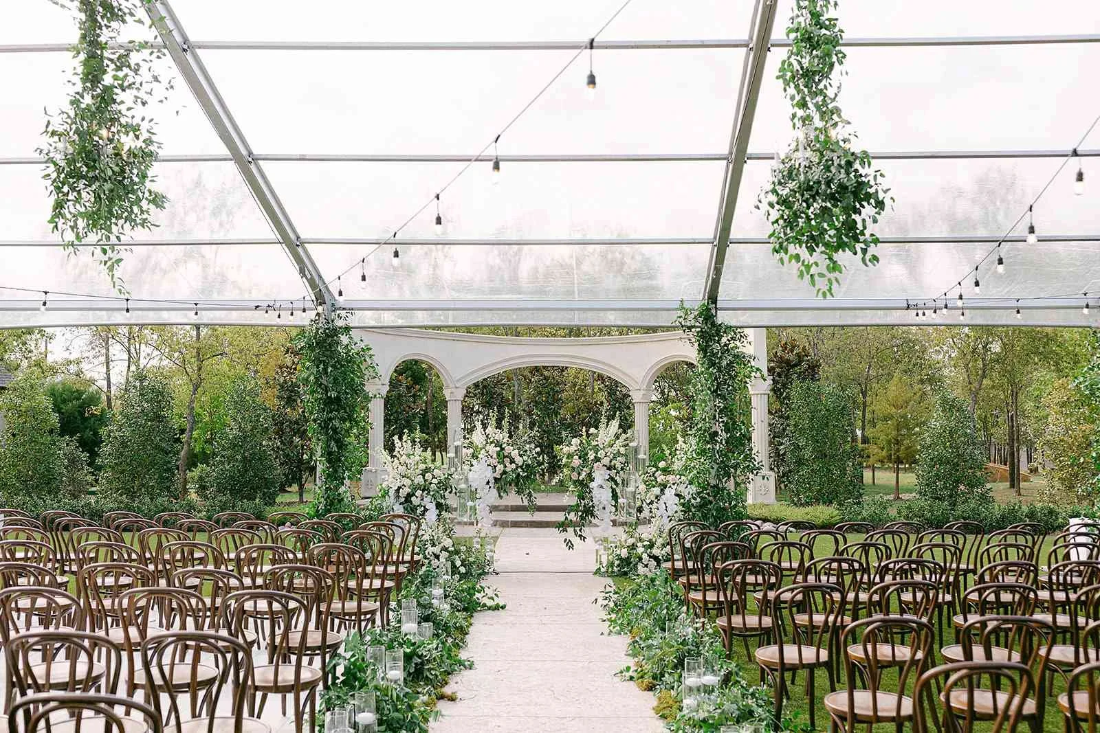 Clear tent wedding ceremony setup at Knotting Hill Place outdoor event venue with  elegant ceremony chairs, ivy and floral decorations, and 300-guest outdoor ceremony  capacity for Dallas-Fort Worth weddings
