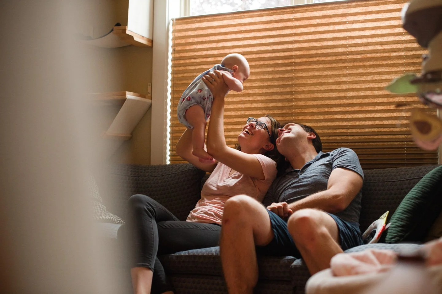 Candid in-home family moment with parents smiling and holding baby – Kellie Henriksen Photography, Denver lifestyle family photographer capturing natural and joyful portraits.