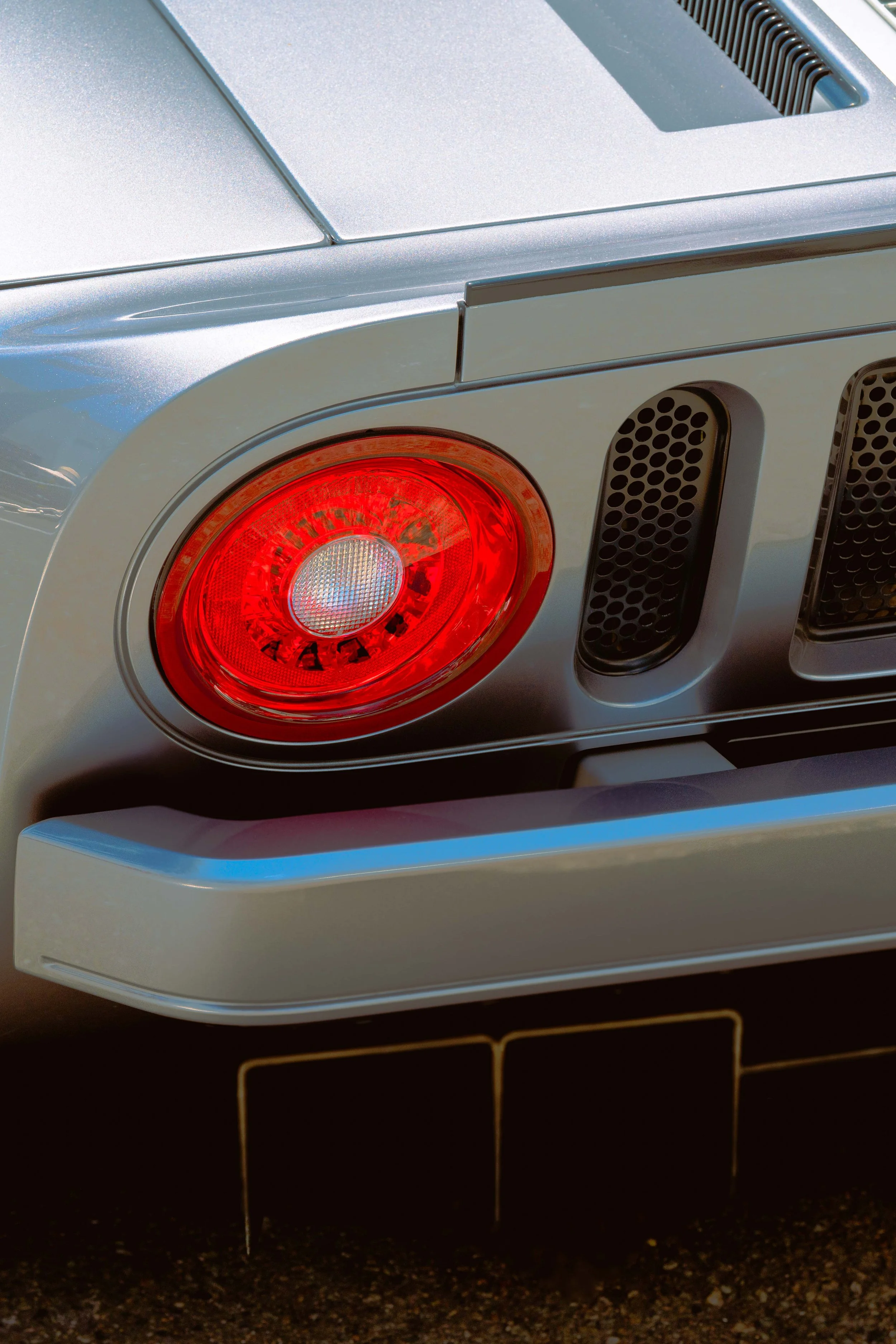 Close-up of the rear of a silver luxury car showing the tail light, part of the trunk, and vents.