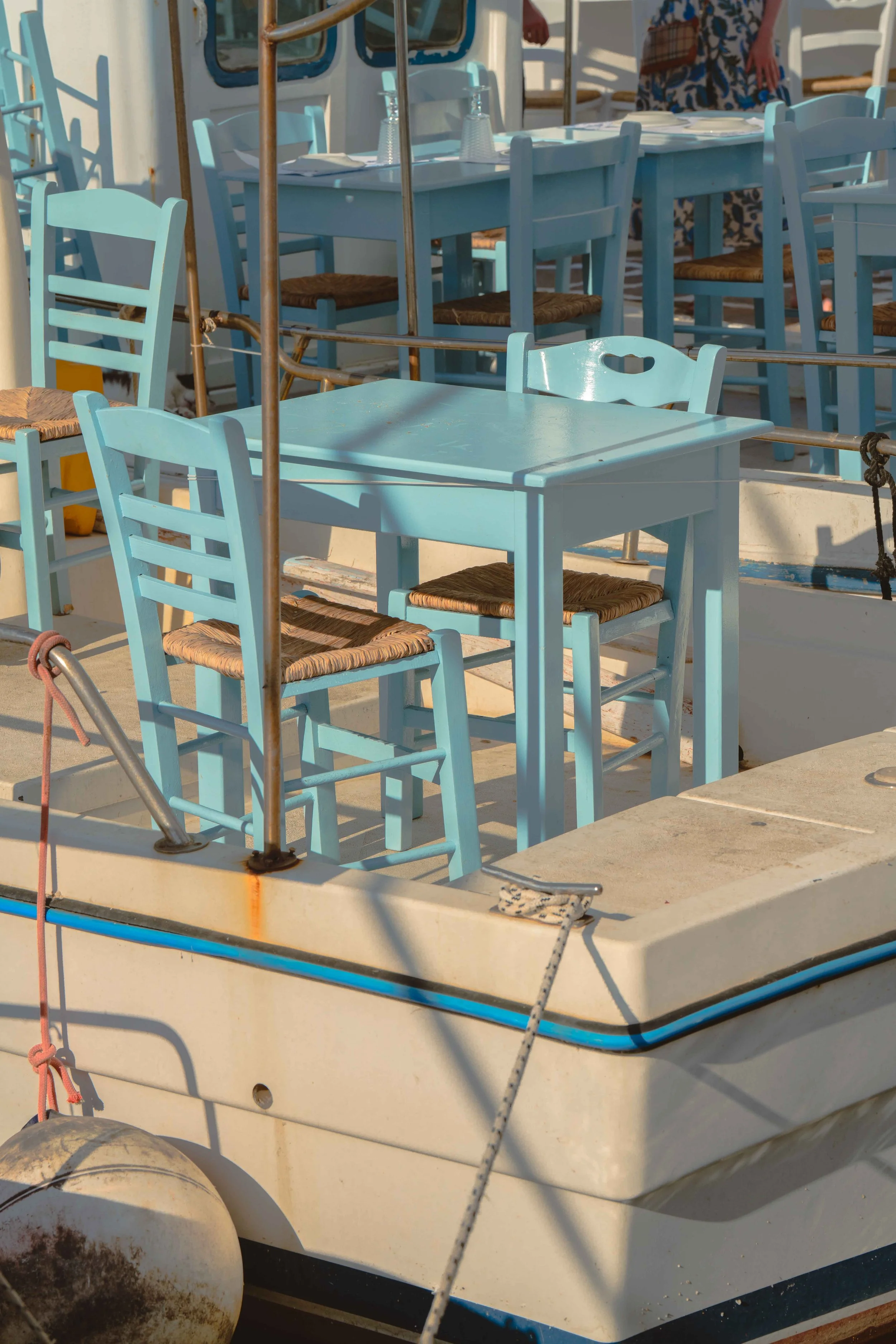 A close-up view of a white boat with light blue chairs and a table, set for dining, with plates and glasses on top. The boat appears to be docked.