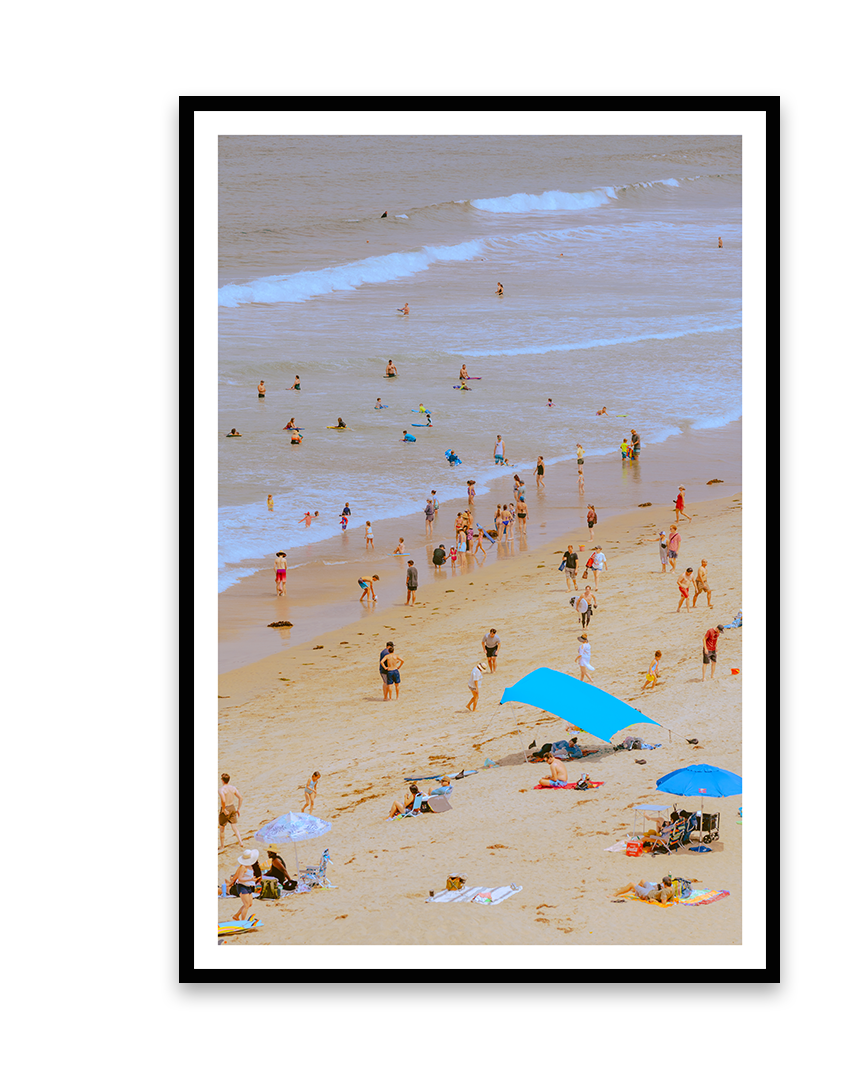 Beach scene with people swimming, wading, and relaxing under umbrellas on sandy shore.