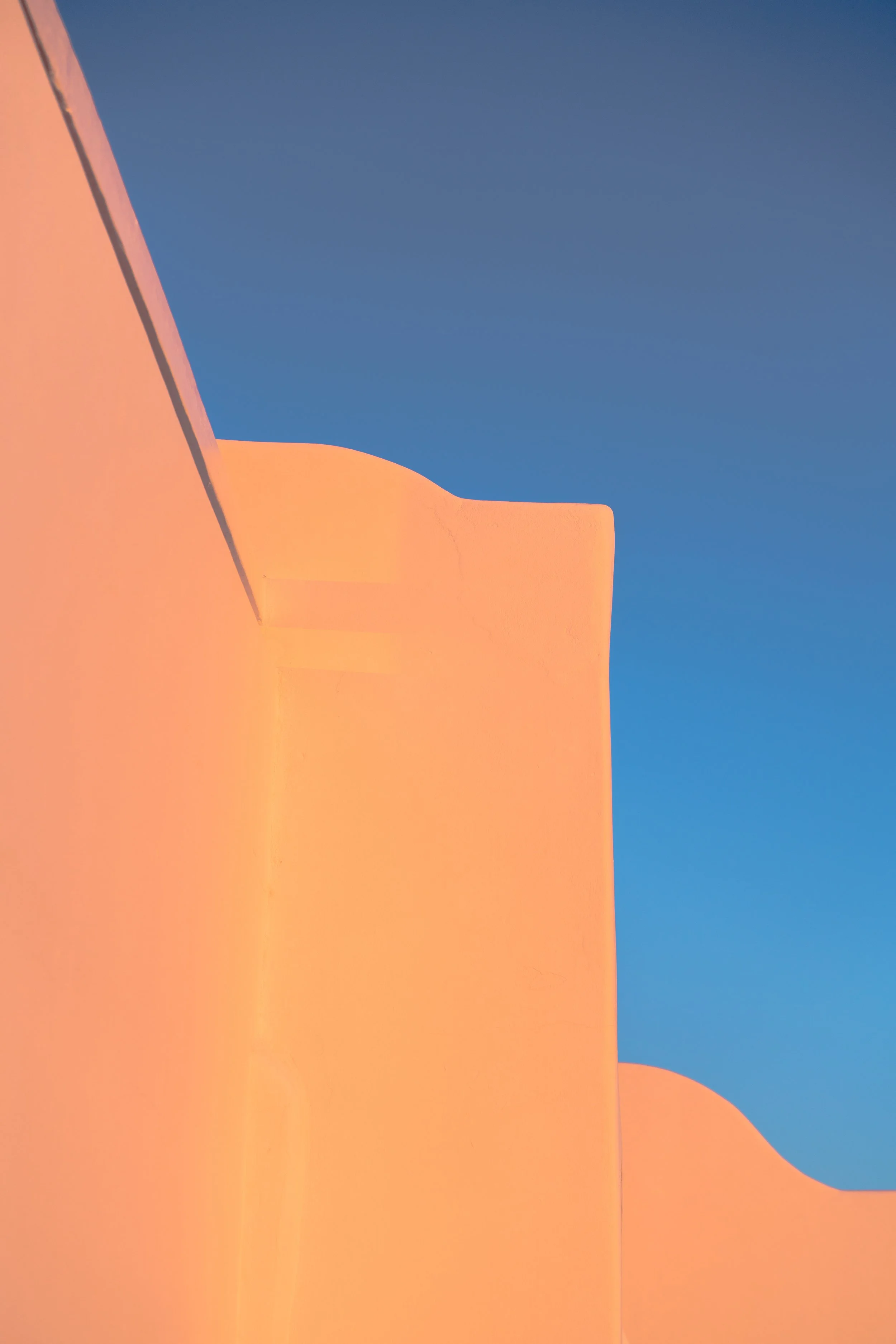 A building with smooth orange-colored walls and unique architectural features against a clear blue sky.