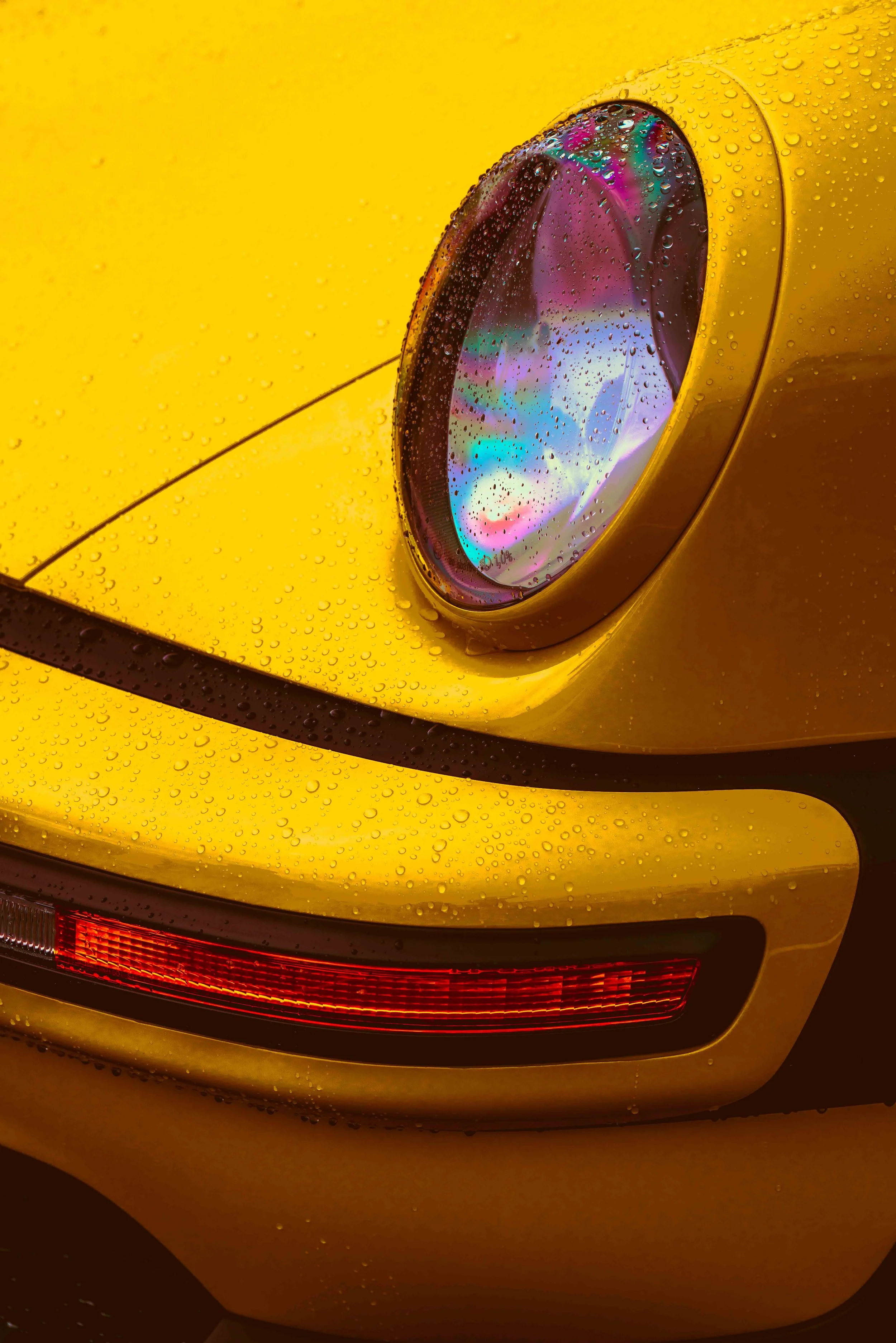 Close-up of a yellow Porsche car's headlight with water droplets on its surface.