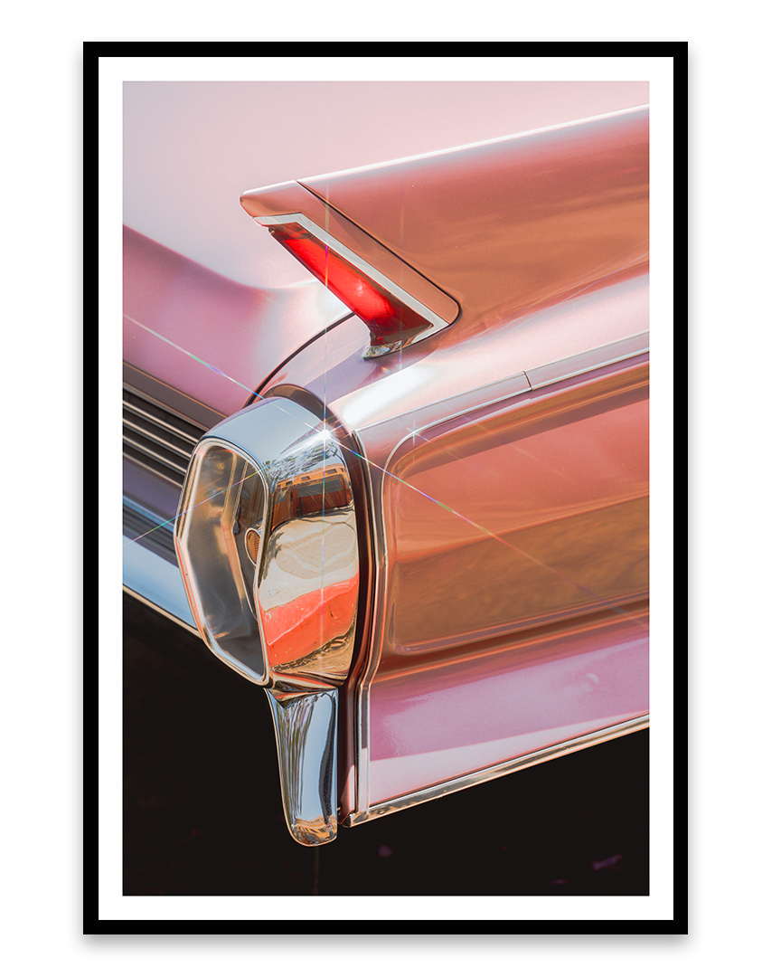 Close-up of the rear end of a vintage pink Cadillac, featuring tail fin with red light and chrome details.