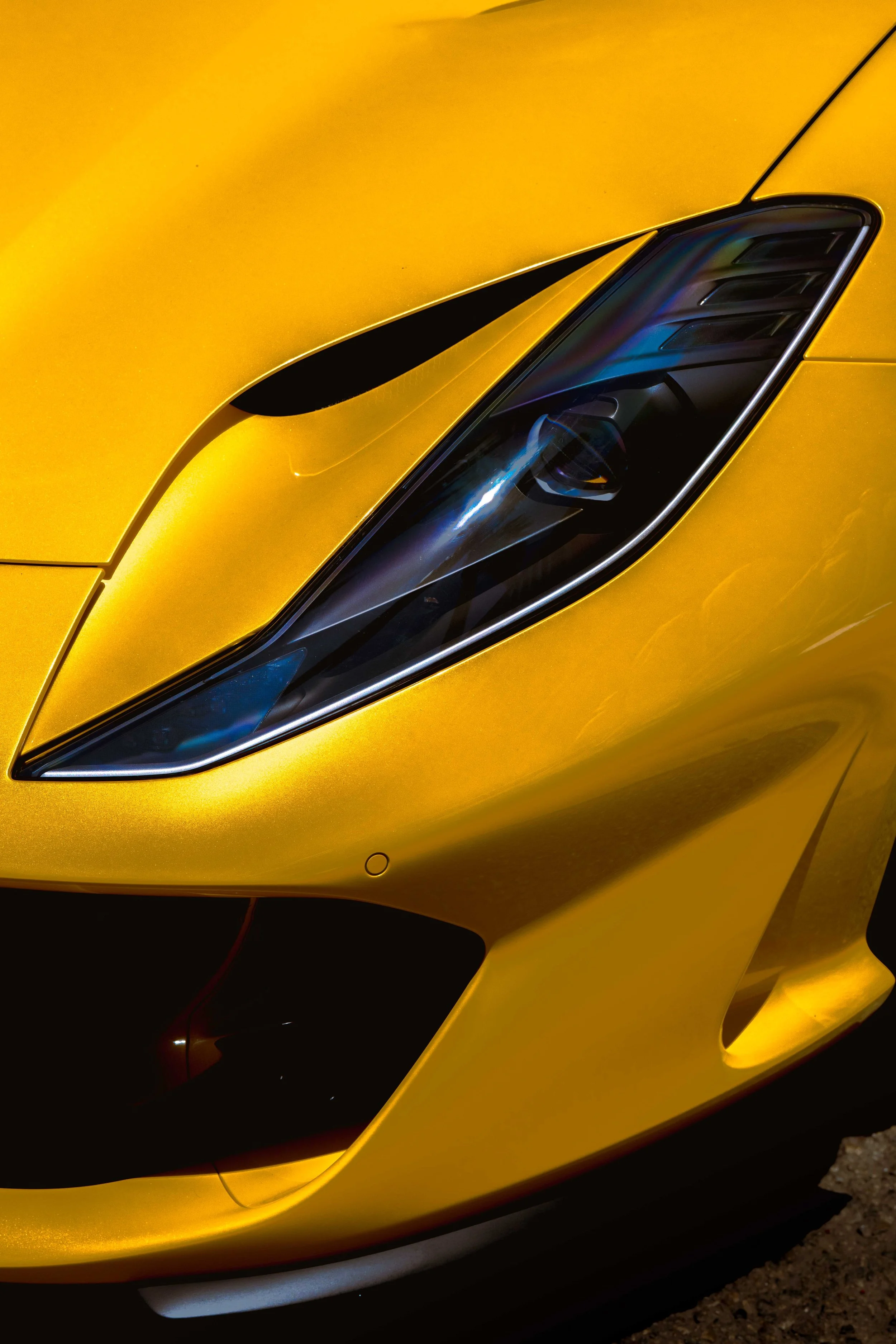 Close-up of a yellow luxury sports car's headlight and front fender.