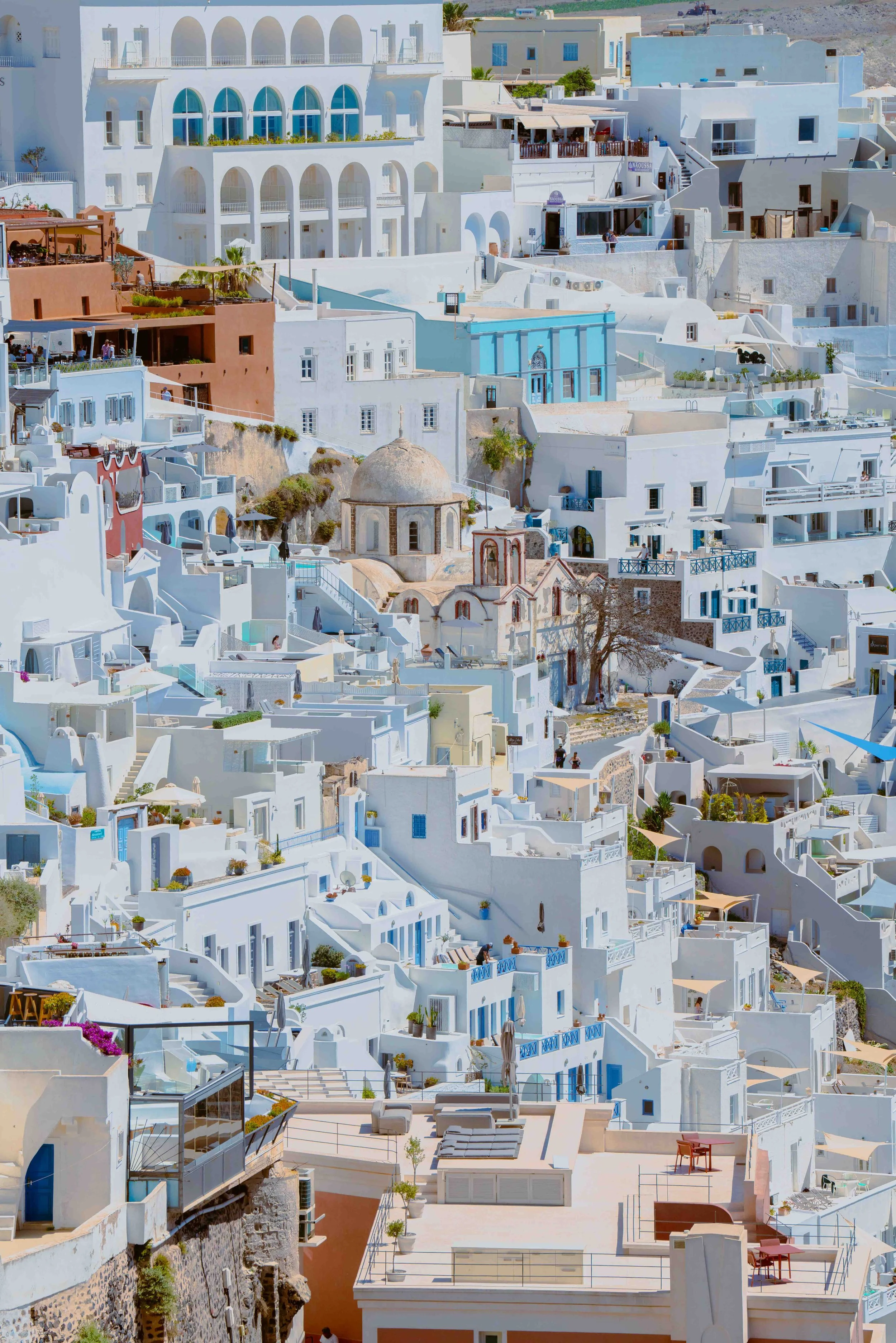 Cluster of white buildings with blue accents and terraces, hillside landscape, traditional architecture in Santorini, Greece.