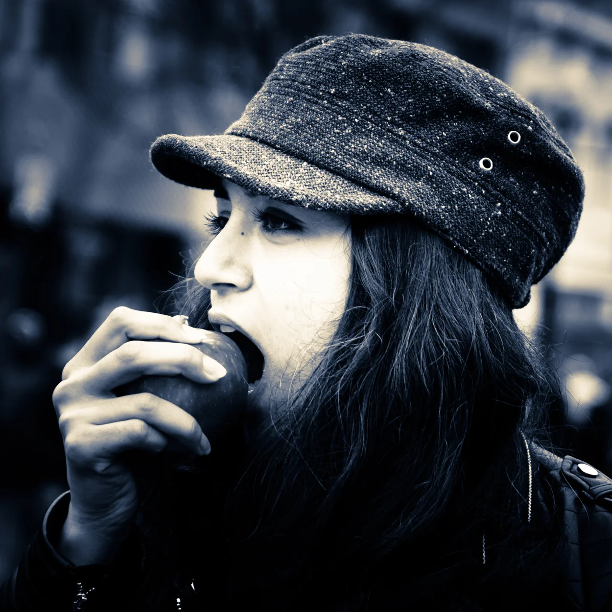 A woman wearing a cap is eating an apple.
