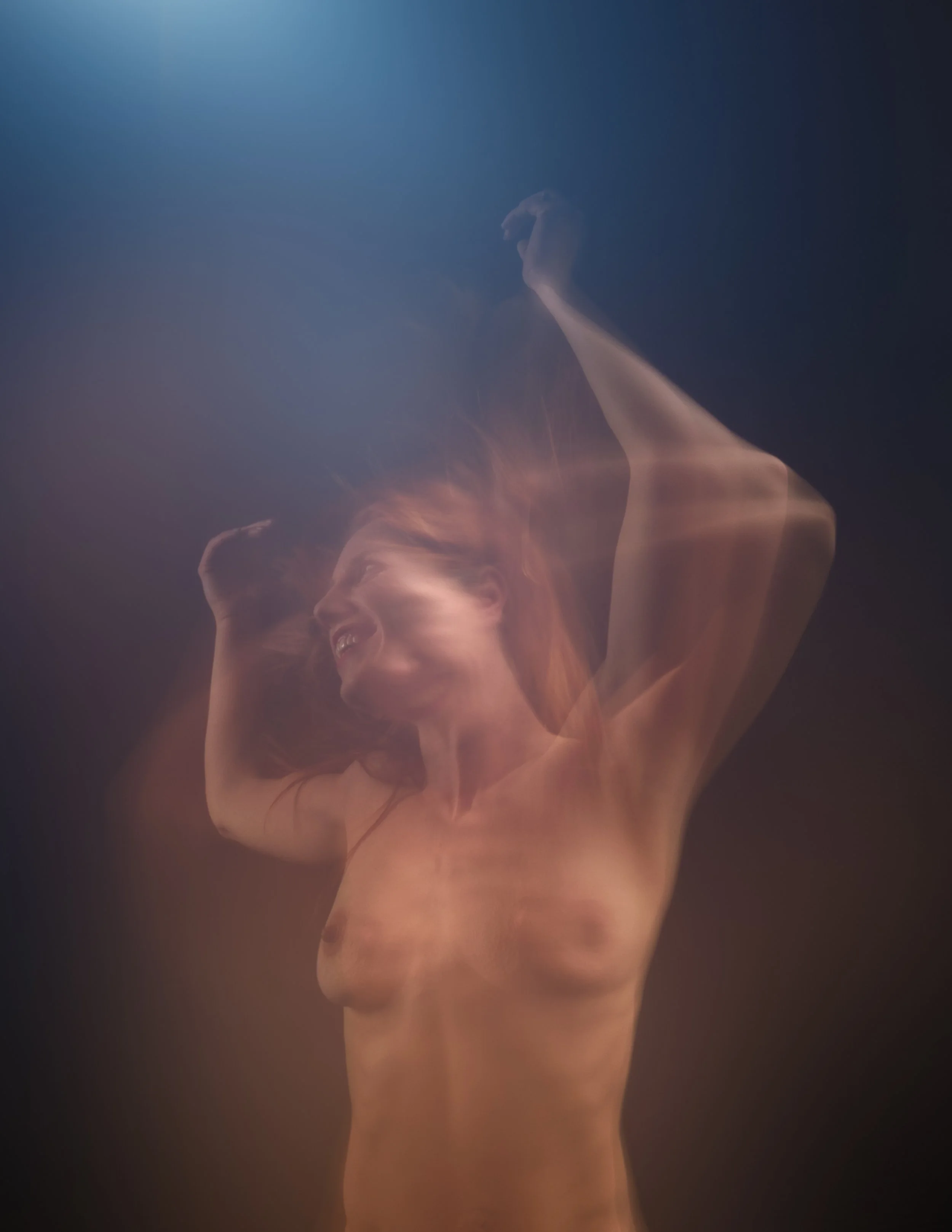 A topless woman with red hair smiling and holding her arms above her head, with a blurred and artistically streaked effect.