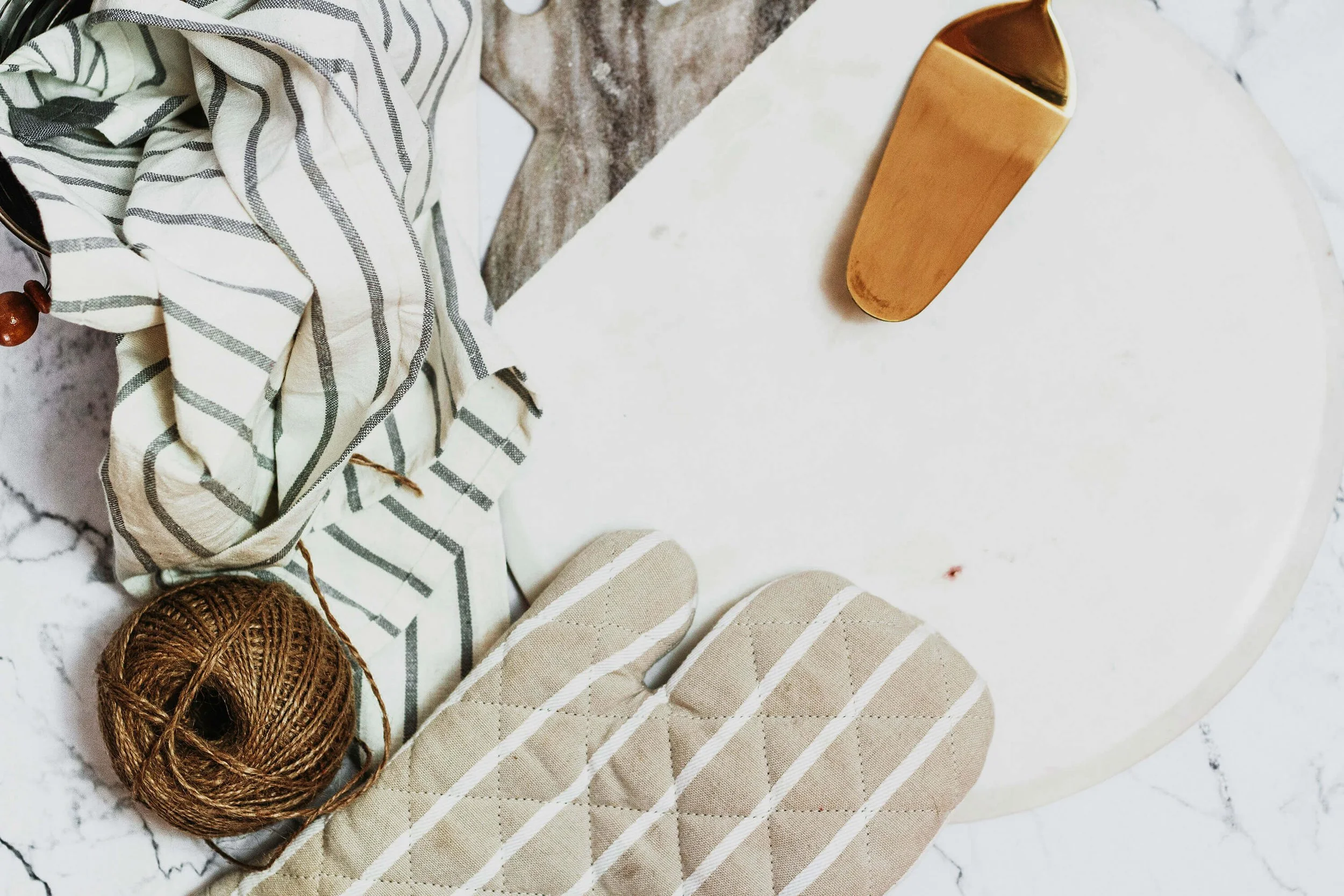 Kitchen countertop with a ball of brown twine, a striped kitchen towel, and an oven mitt.
