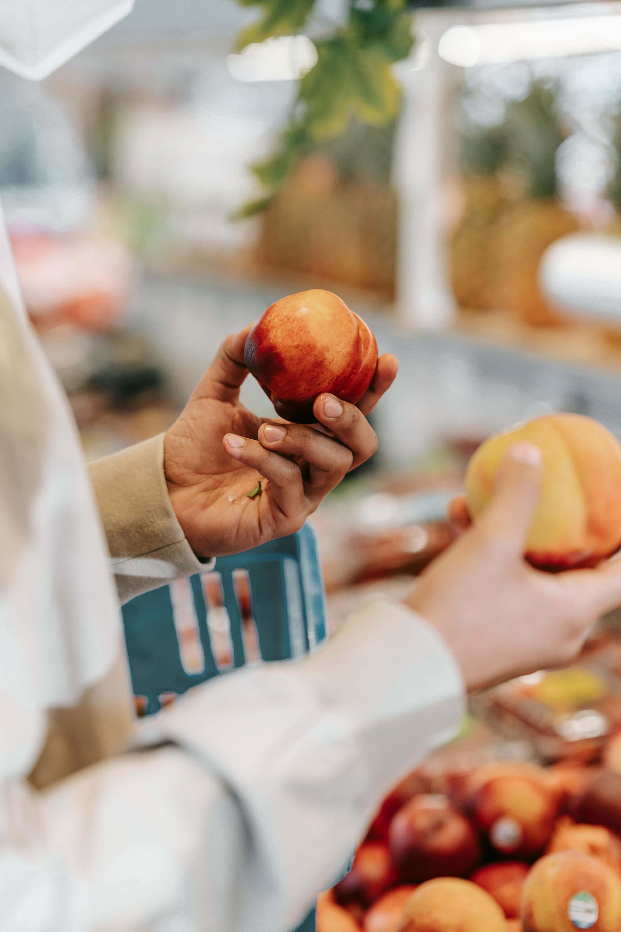 Person holding a red and yellow peach in a grocery store.