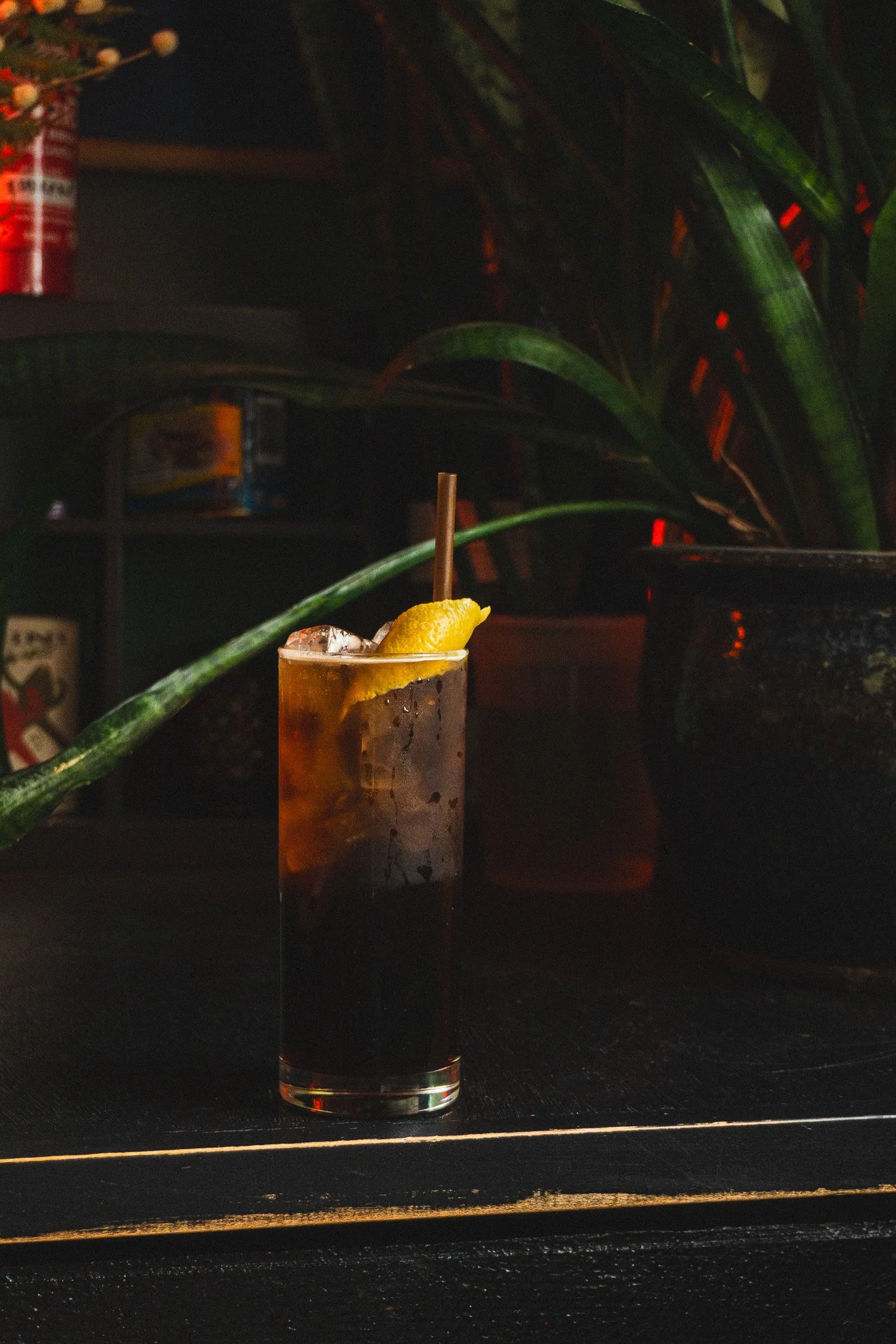 A glass of cola with ice, a lemon wedge and a straw on a dark wooden surface.