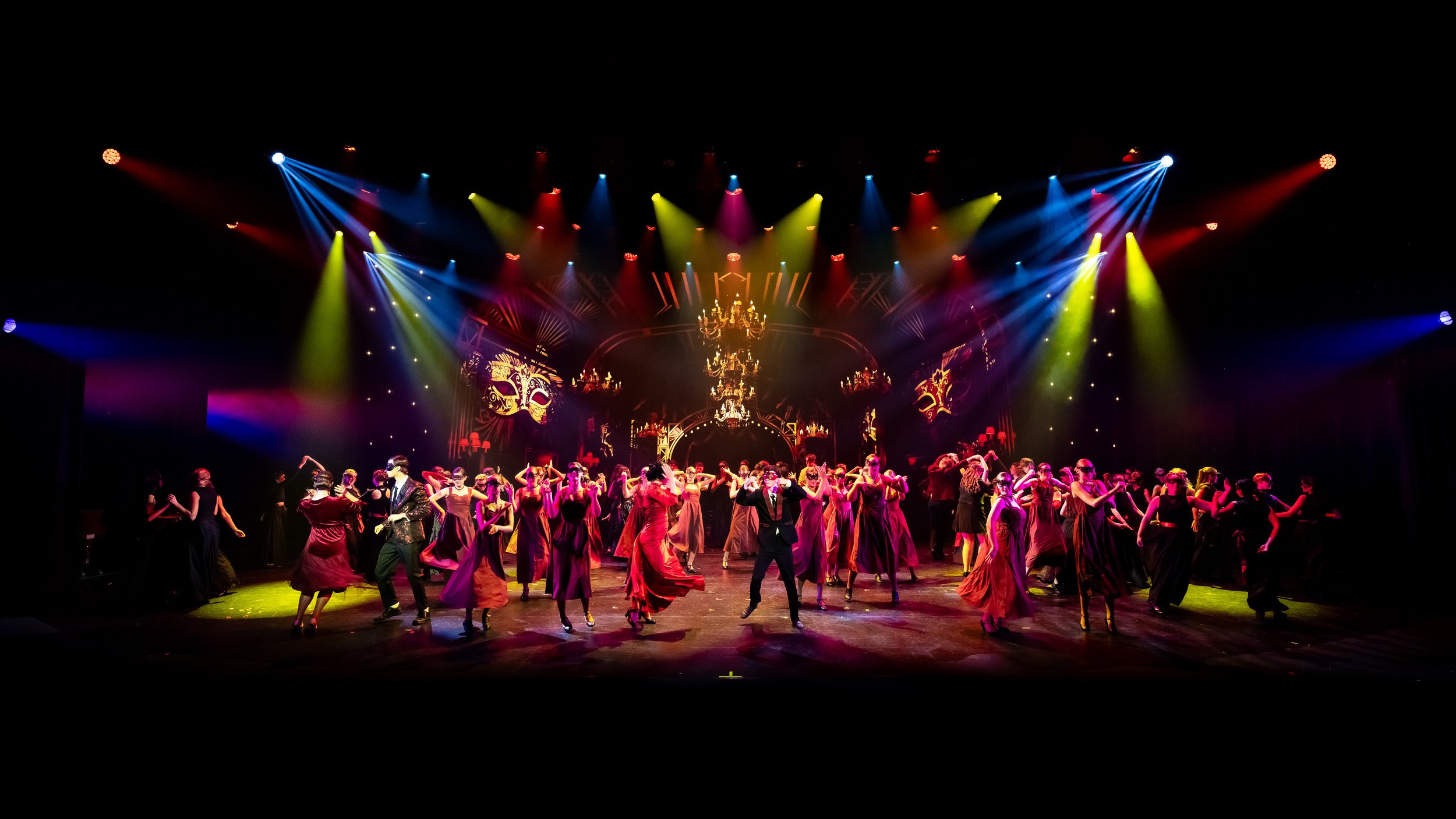 A stage performance featuring dancers in formal attire, with colorful lighting and decorative backdrop.