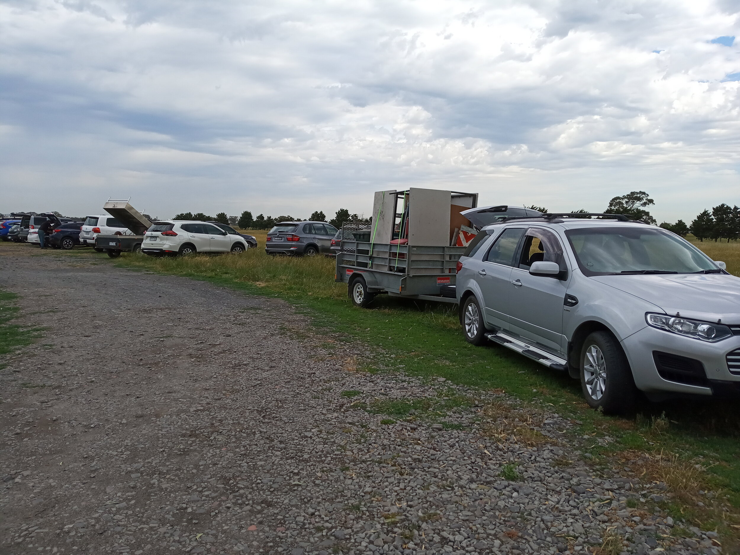  28/11  Shot of some of the cars lined up at the working bee. Bill S’s trailer load of tables, chairs and more in the foreground 