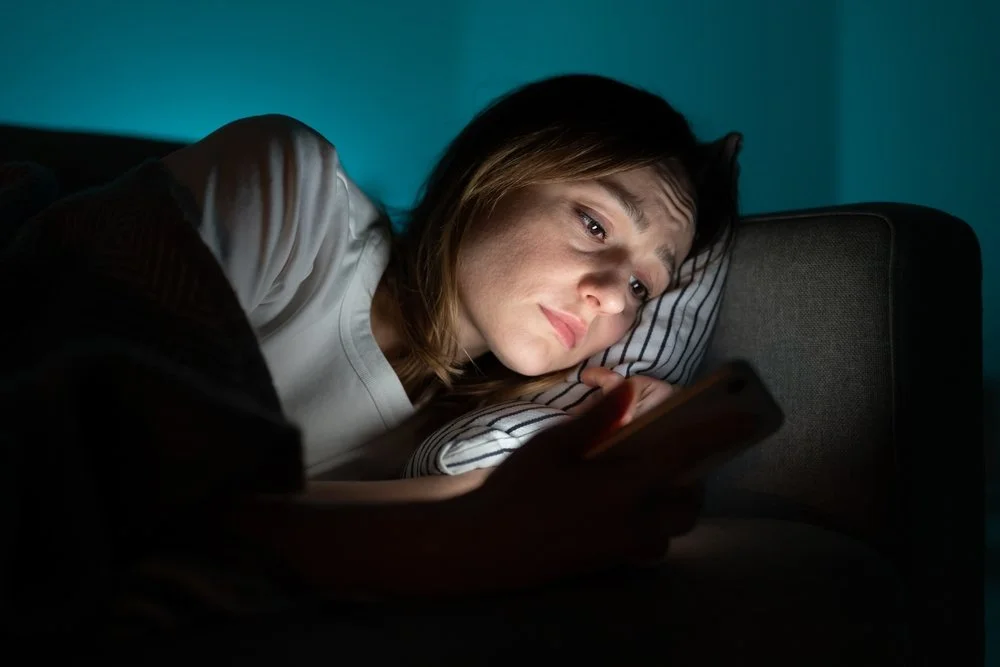 woman laying in bed on her phone looking upset