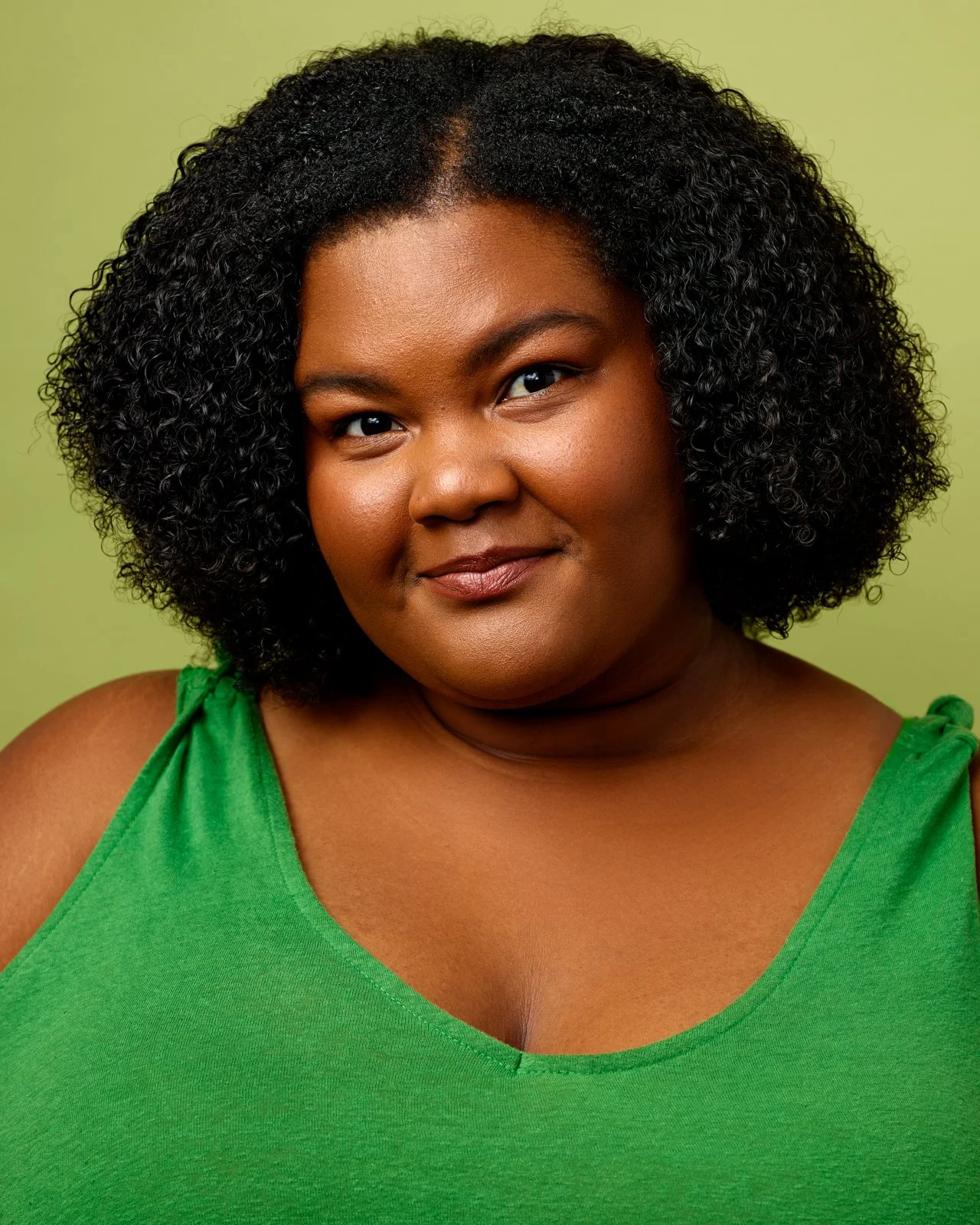 A high-quality actor headshot of a woman in a green top, demonstrating a natural and polished look for agent submissions in Toronto.