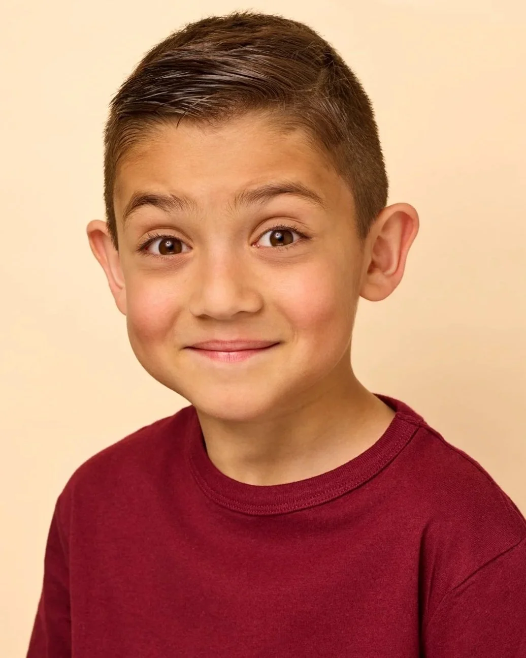 A professional youth theatrical headshot of a boy in a burgundy shirt, featuring a natural and engaging expression.