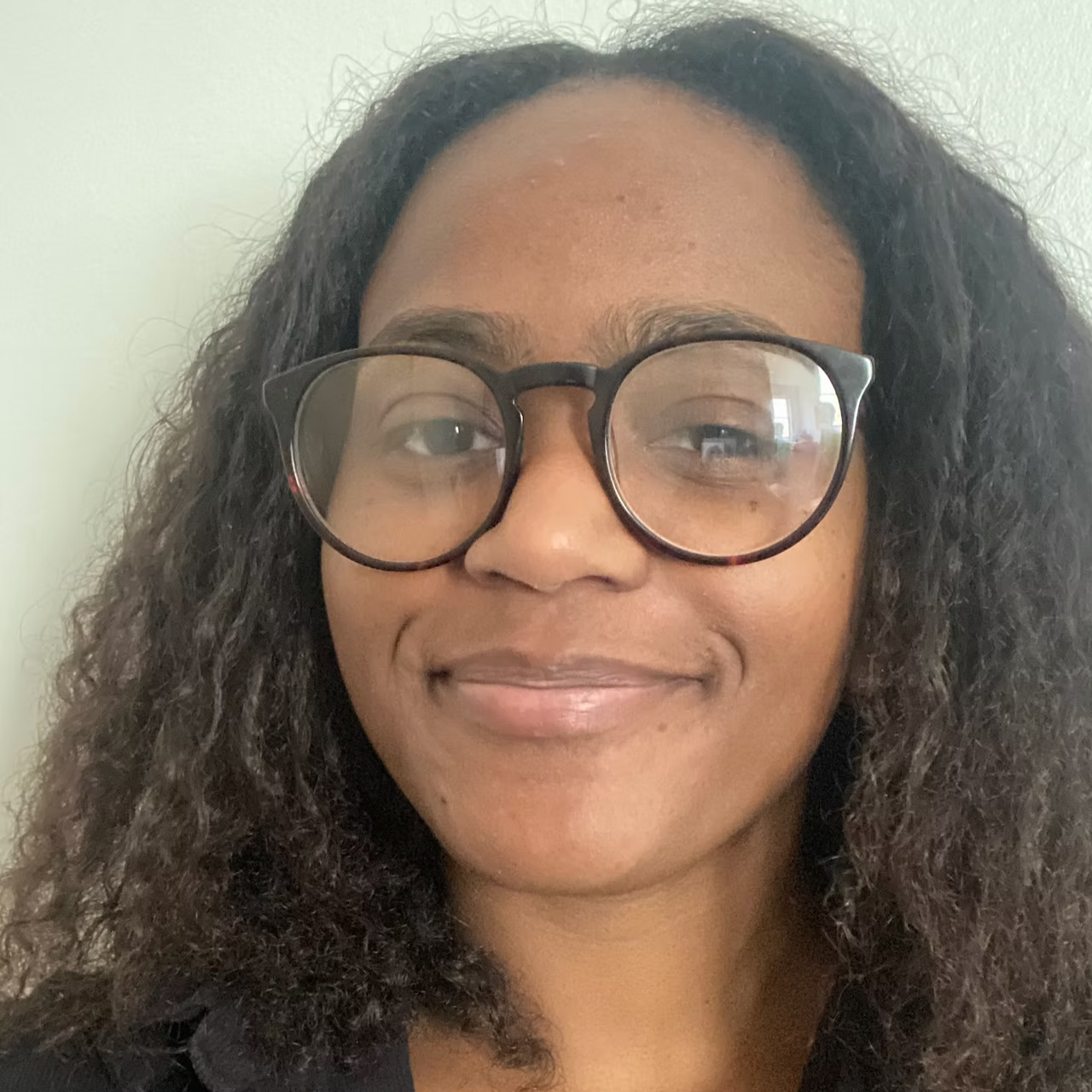 A woman with curly hair wearing black-rimmed glasses smiling at the camera.