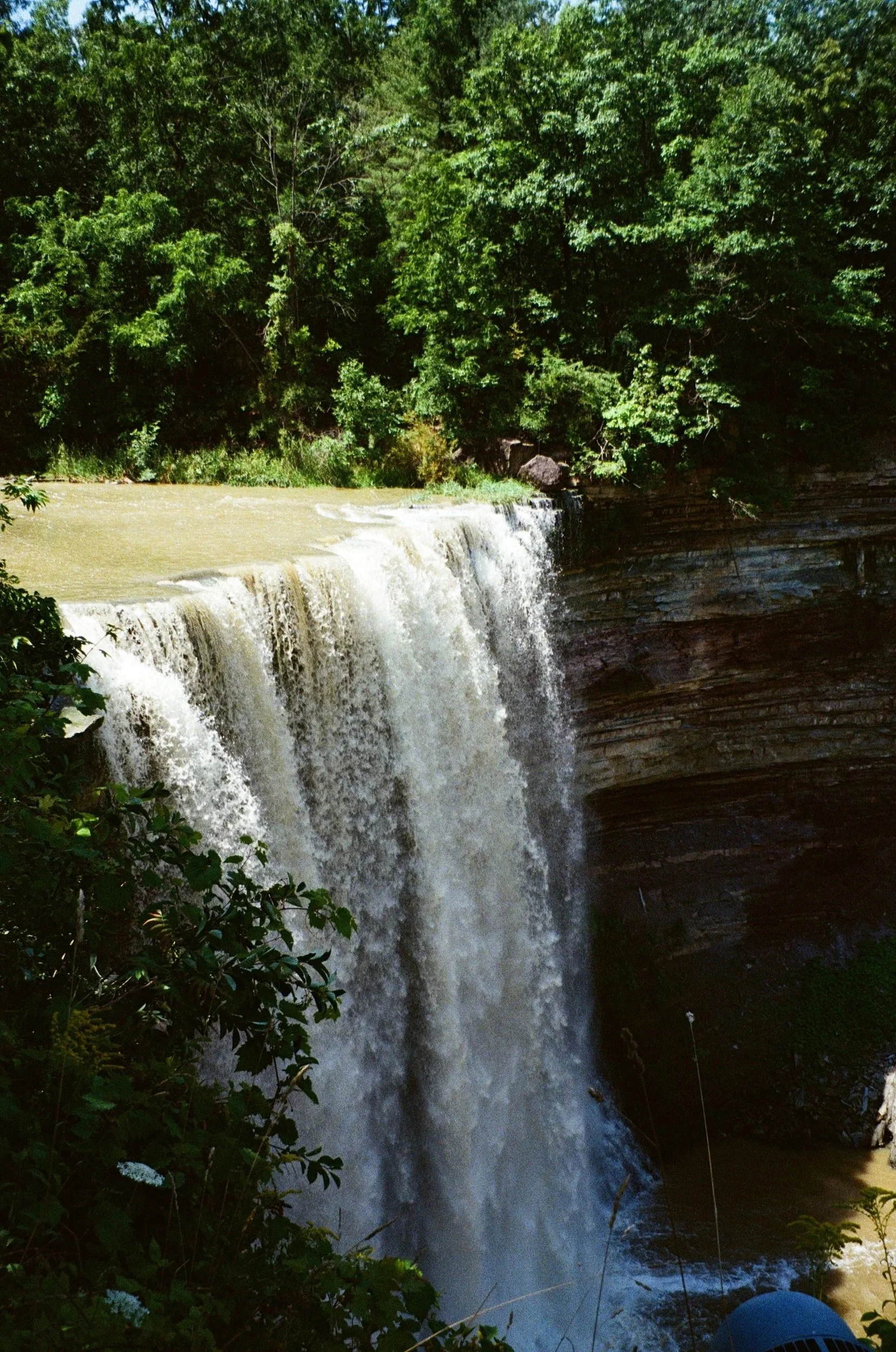 A waterfall flowing over rocks with lush green trees surrounding it.