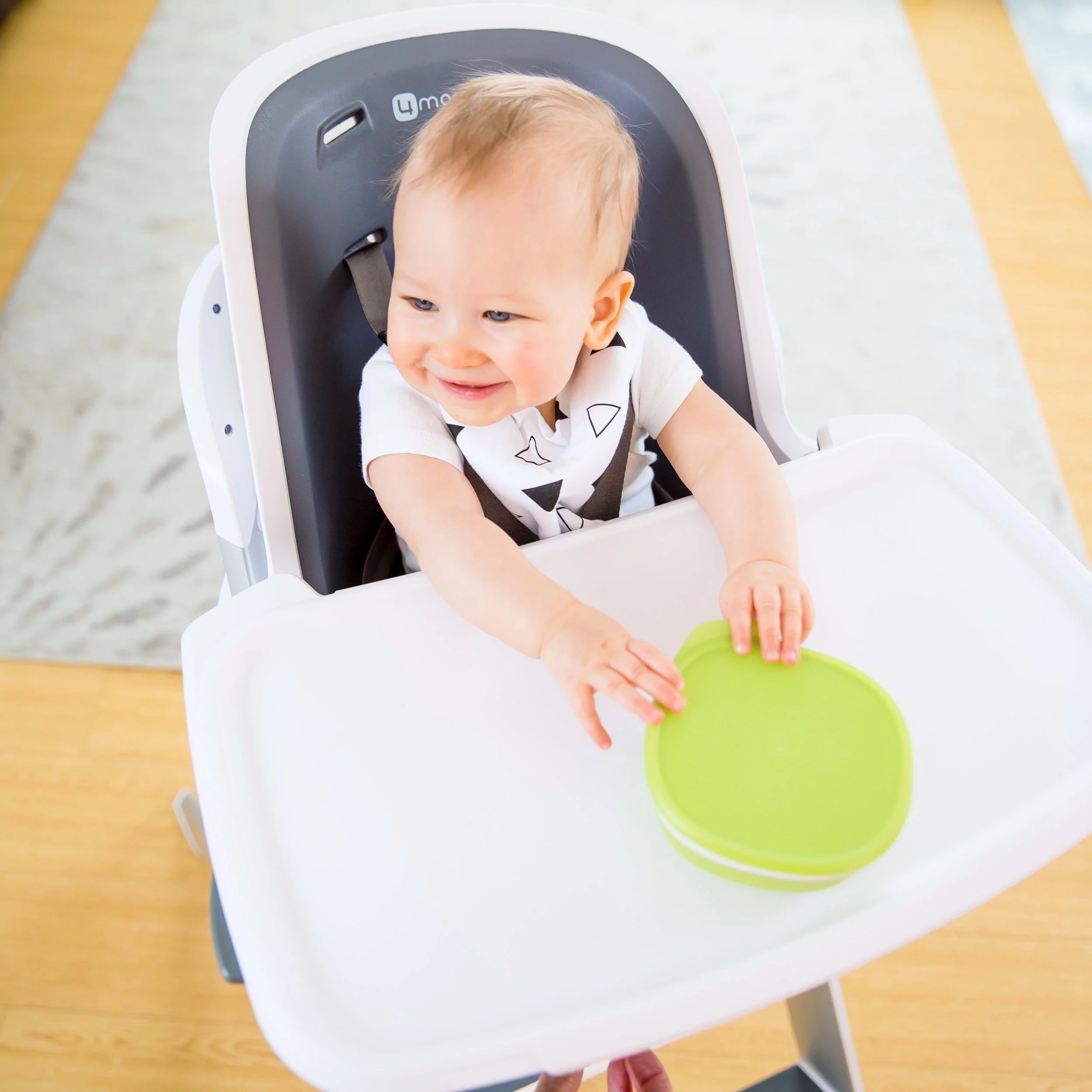 A young baby sitting in the best high chair holding a green bowl