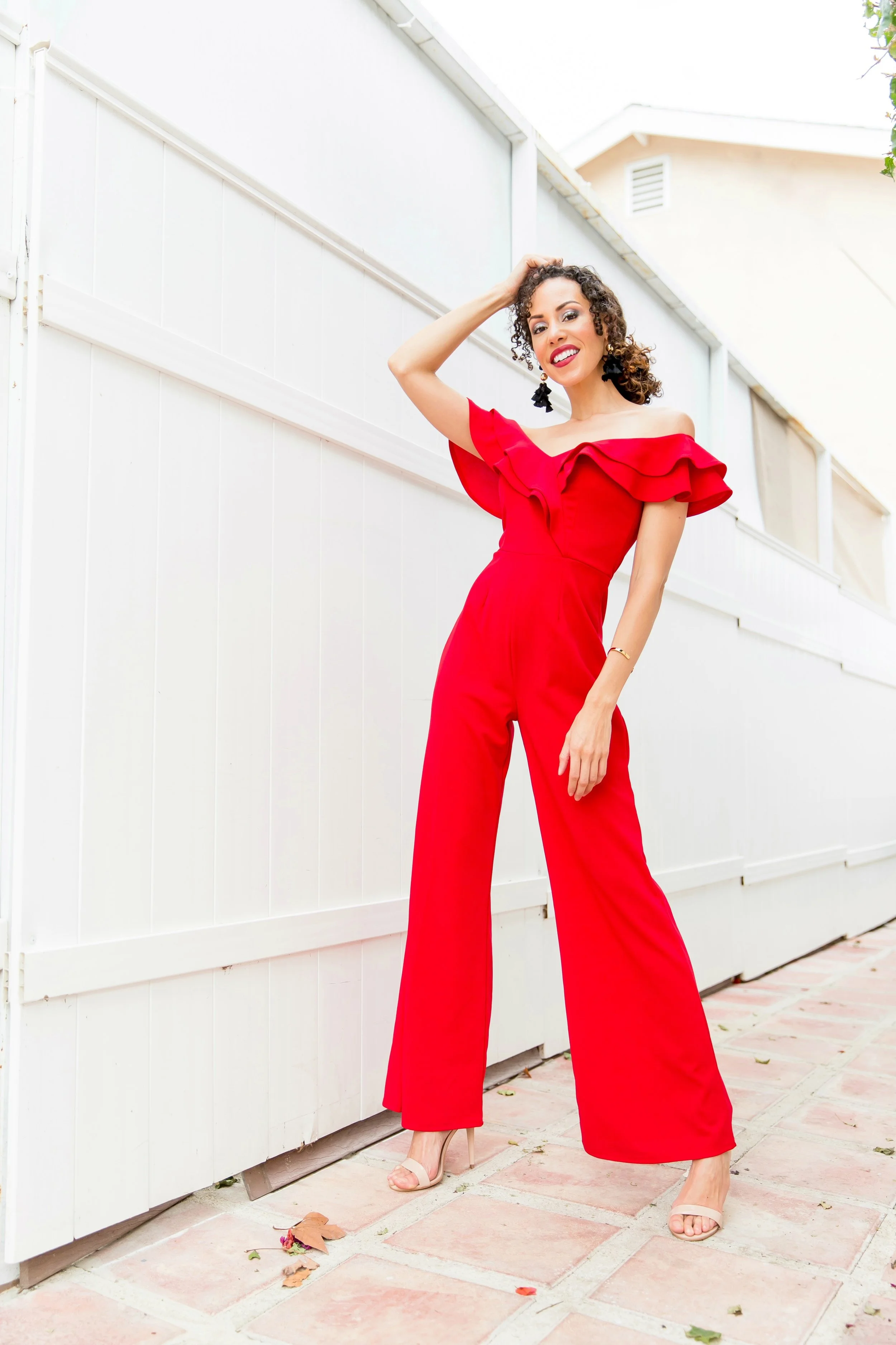 Woman in a red, ruffled jumpsuit in front of a tall white fence
