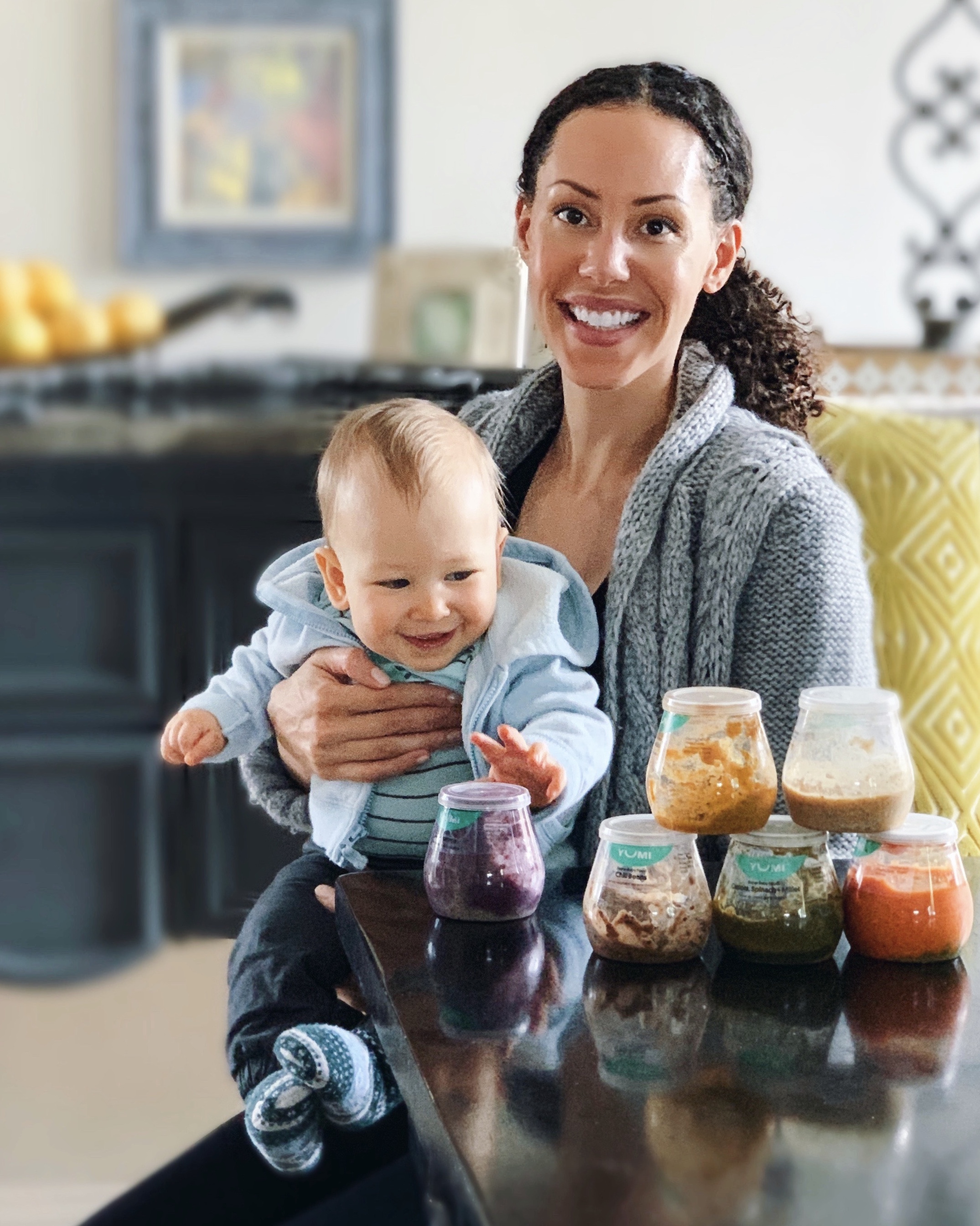 Mother and happy baby sitting at a table with Yumi Baby Food containers