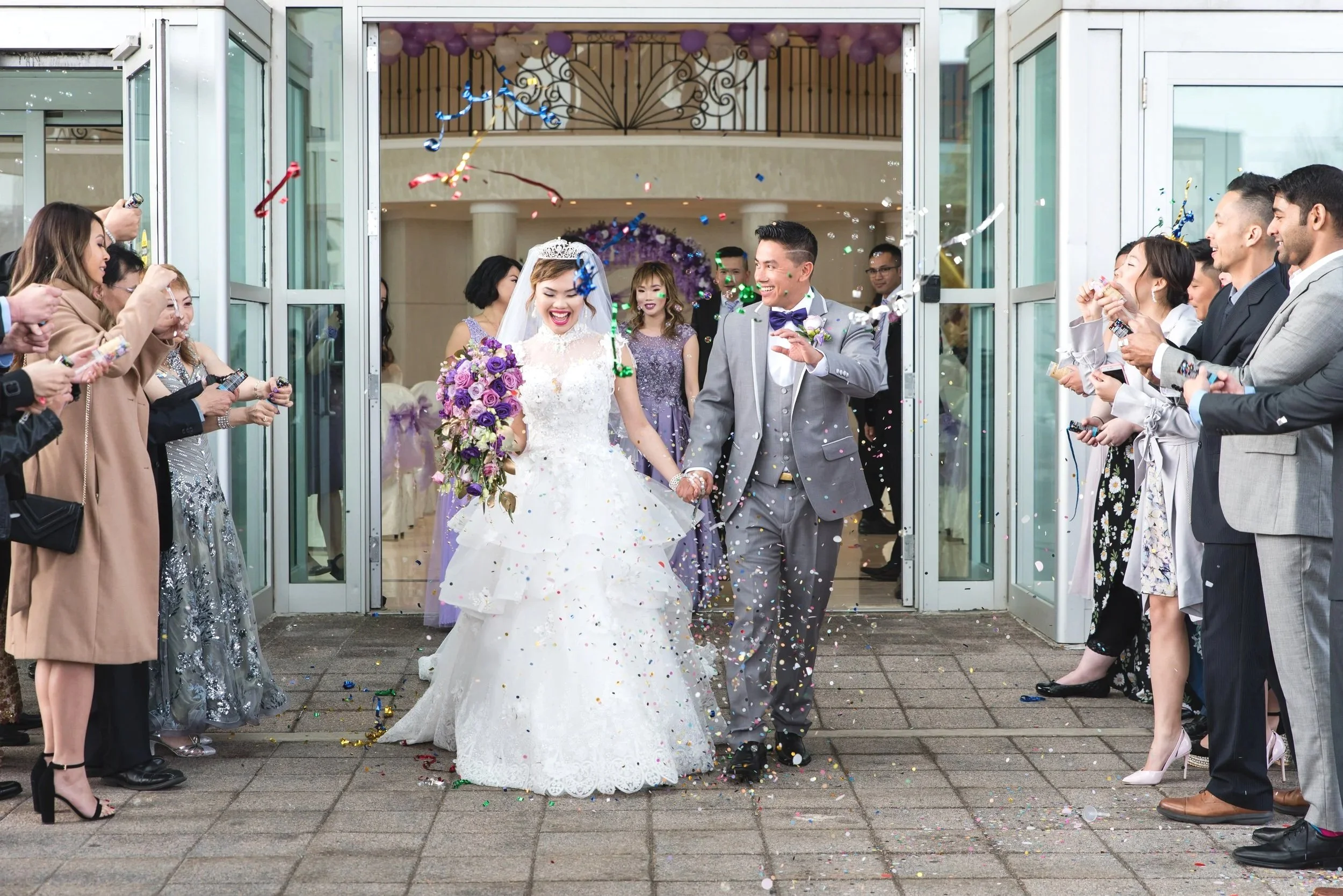 Bride and groom walking through a confetti exit while celebrating with their wedding guests.