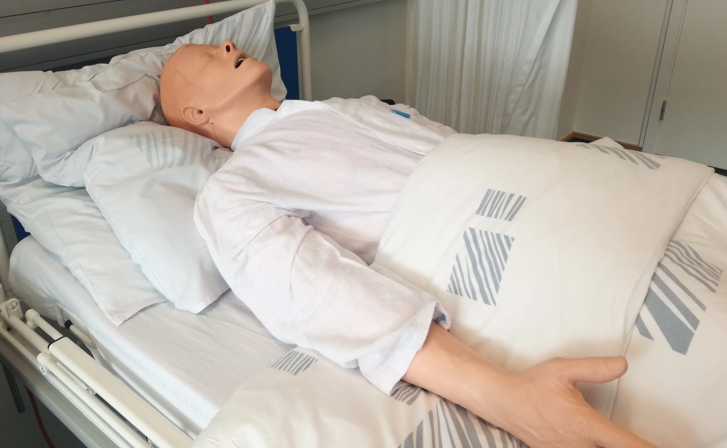 En simulationsdukke ligger i en hospistalsseng.