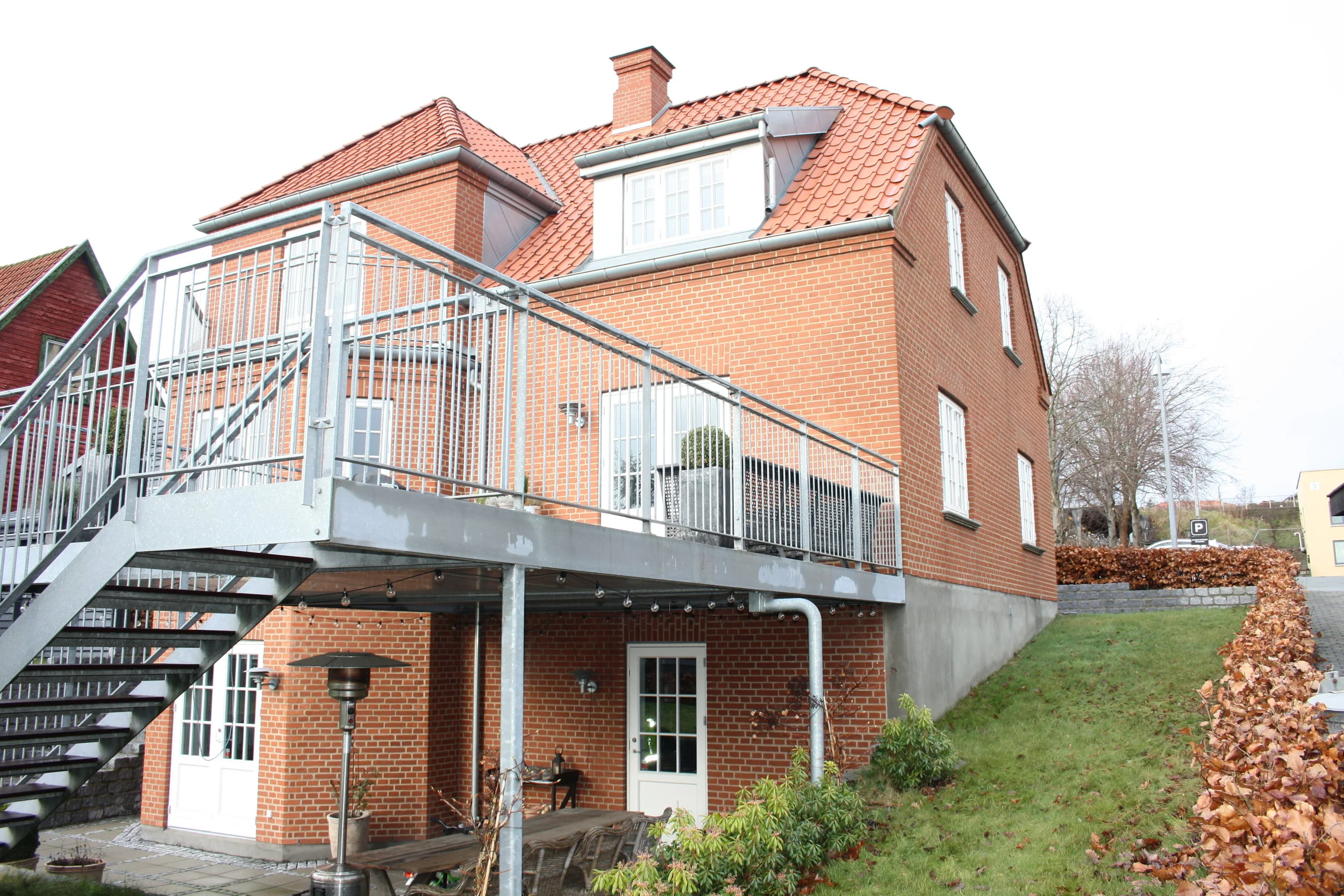 Stor terasse på havesiden, blev indtænkt så lys kunne trænge ind til kælder etagen.  Direkte adgang fra køkken/spise afdeling.  Overdækning fungere samtidig i dårligt vejr, fra underliggende etage. 
