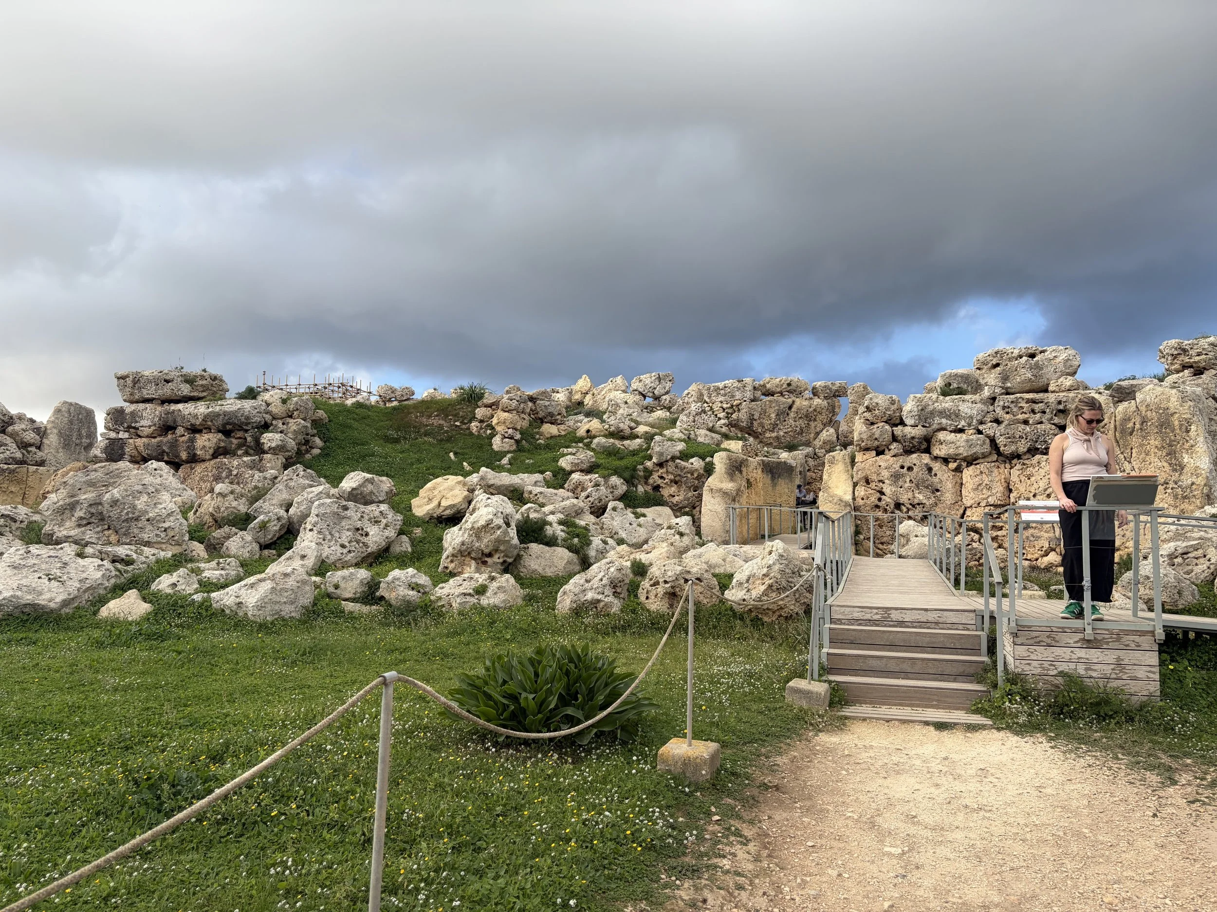 Woman reads a sign at Temples of Ggantijia beneath a moody sky