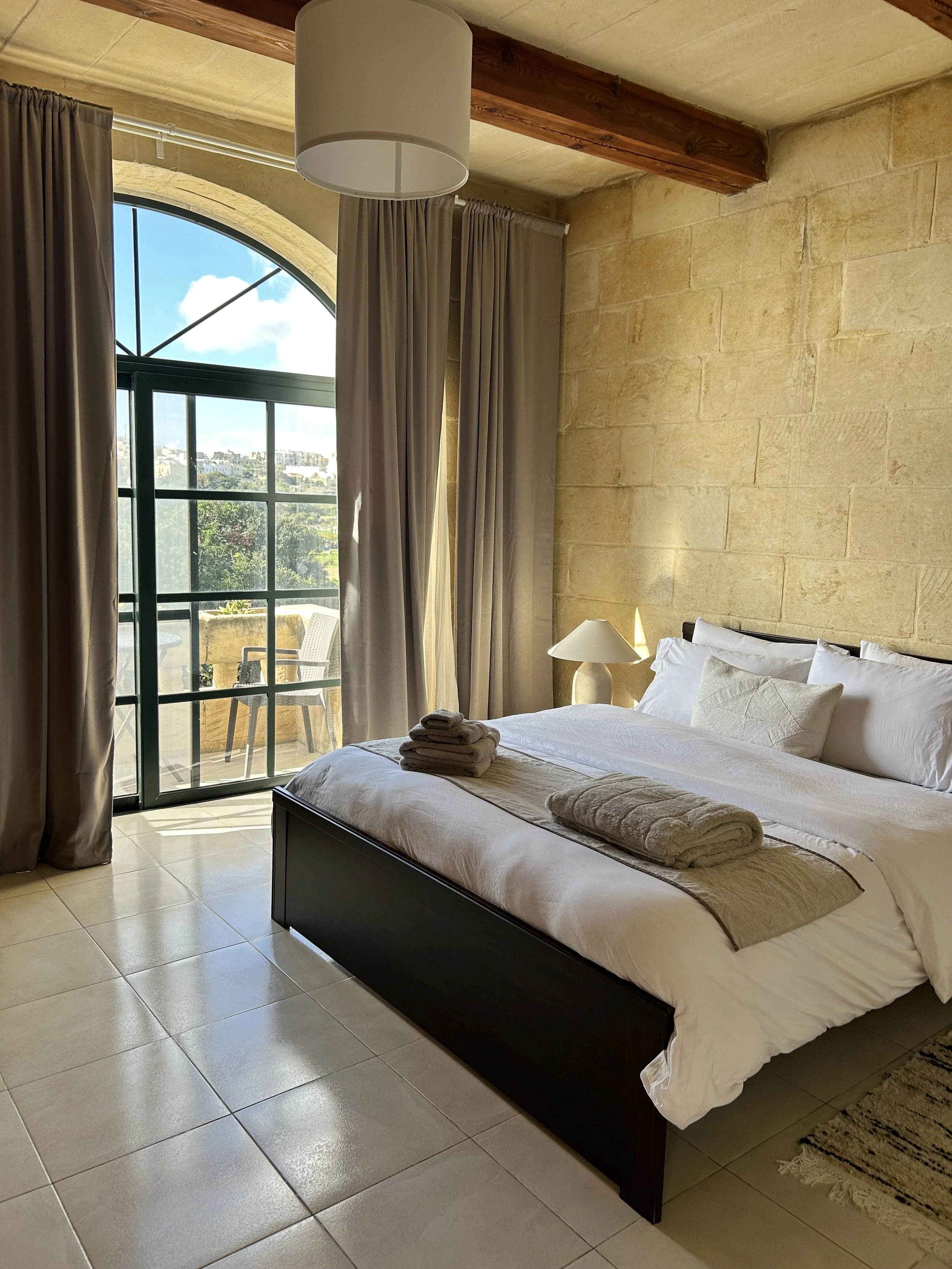 Stylish bedroom showing double bed in front of sandstone wall and lead frames balcony doors