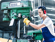 A person wearing safety headphones and gloves working with a large green industrial machine in a factory setting.