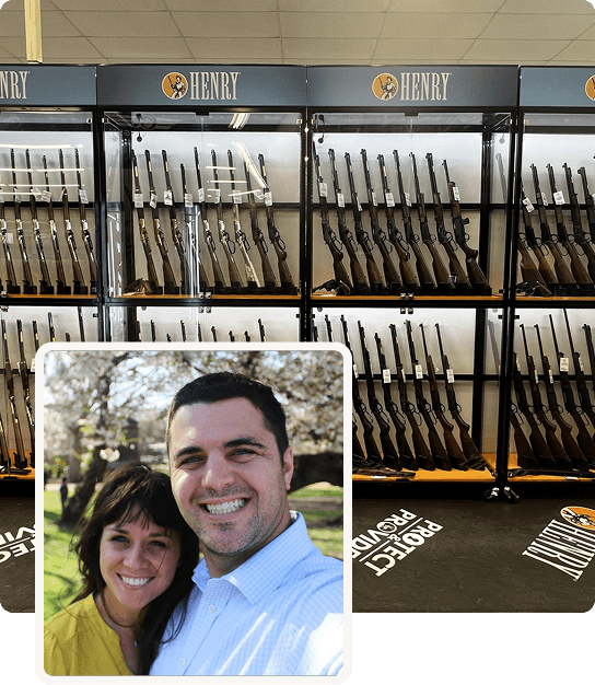 Display of rifles in a gun store with a selfie of a smiling man and woman in front.