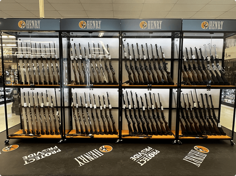 Display of rifles on black metal shelves in a store, branded 'Henry'.