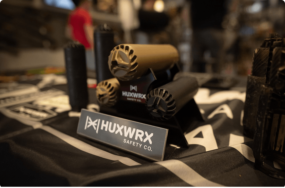 Automotive safety equipment display on table, including flameless lighters with beige and black finishes, branded HUXWRX SAFETY CO, and a sign with the same brand name.