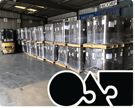 Warehouse with large pallets of glass sheets wrapped in plastic, stacked on wooden pallets, with a forklift in the background.
