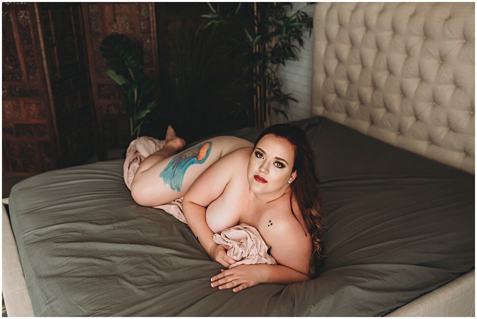 Curvey redhear laying naked with a pink blanket on grey sheets