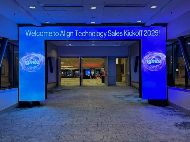 Entrance to a conference with a blue digital sign reading 'Welcome to Align Technology Sales Kickoff 2025!' and Ignite branding on each side.
