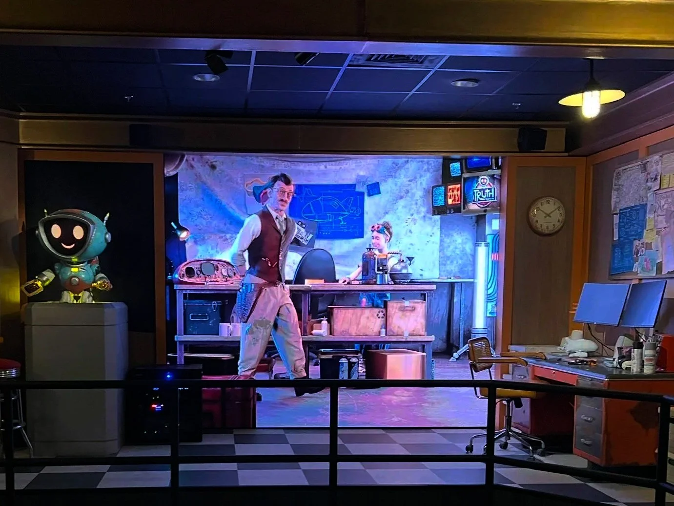 A scene from the animated movie 'Belle' featuring a humanoid robot with a smiling face on the left, a man with glasses and messy hair in the center, and a woman with a bun in the background at a futuristic laboratory with electronic equipment and neon signs.