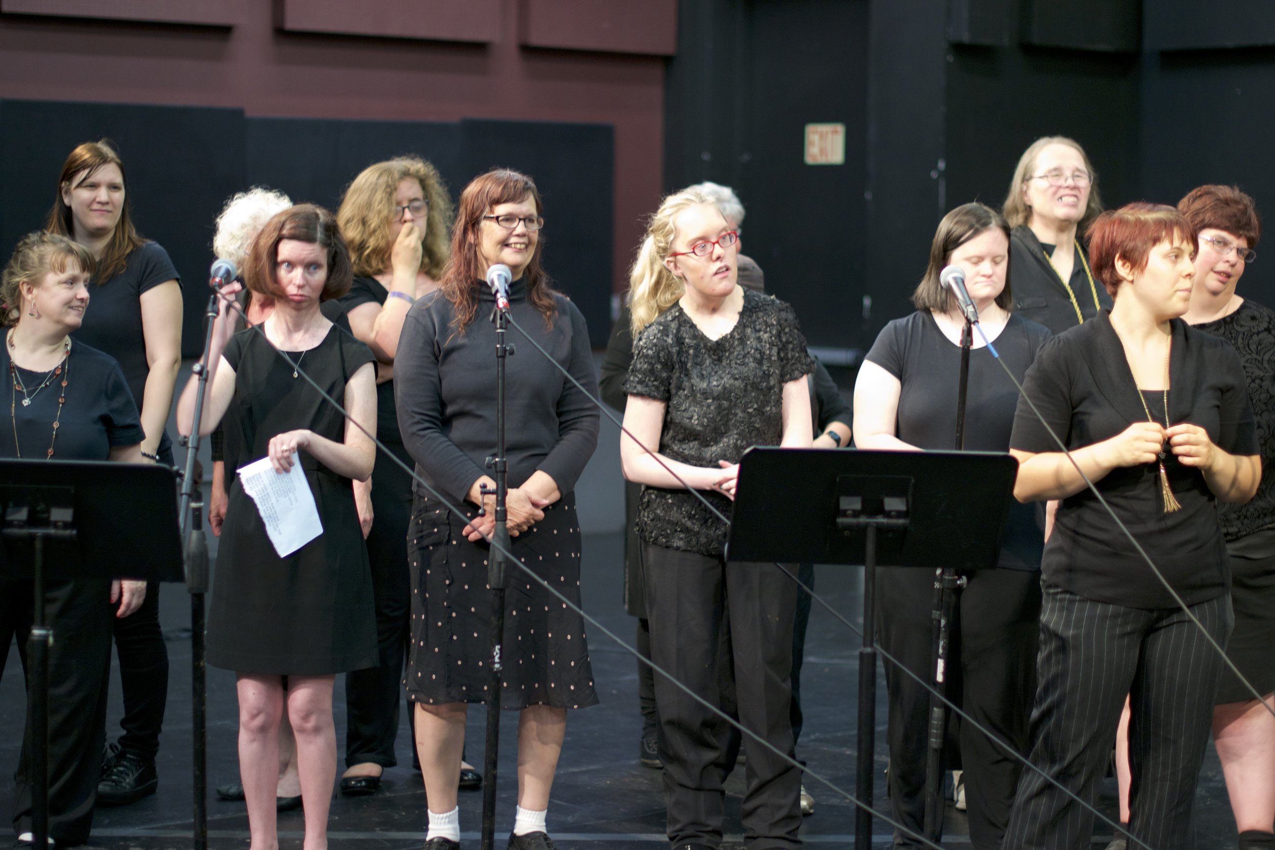 Group of women stand in front of microphones and a music stand