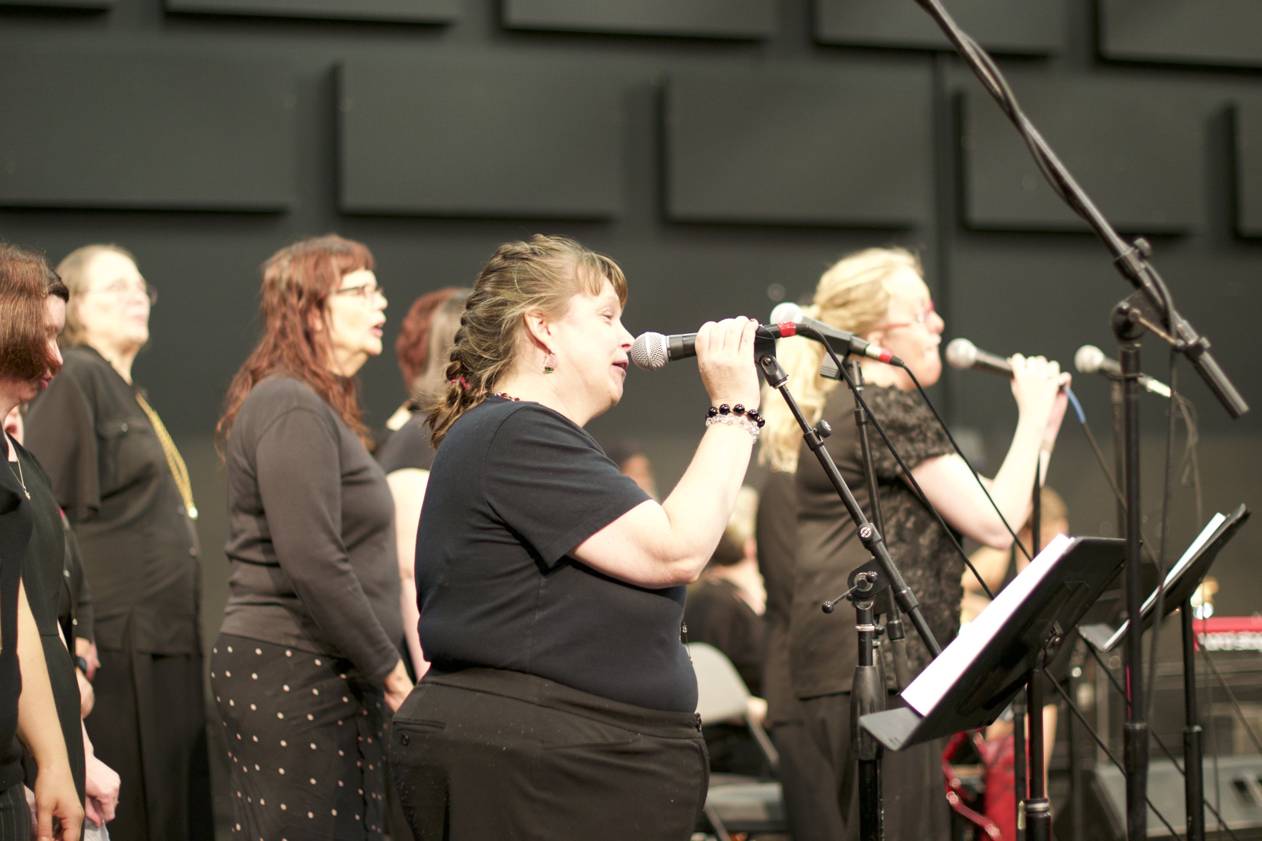 Group of women facing to the side and singing into microphones