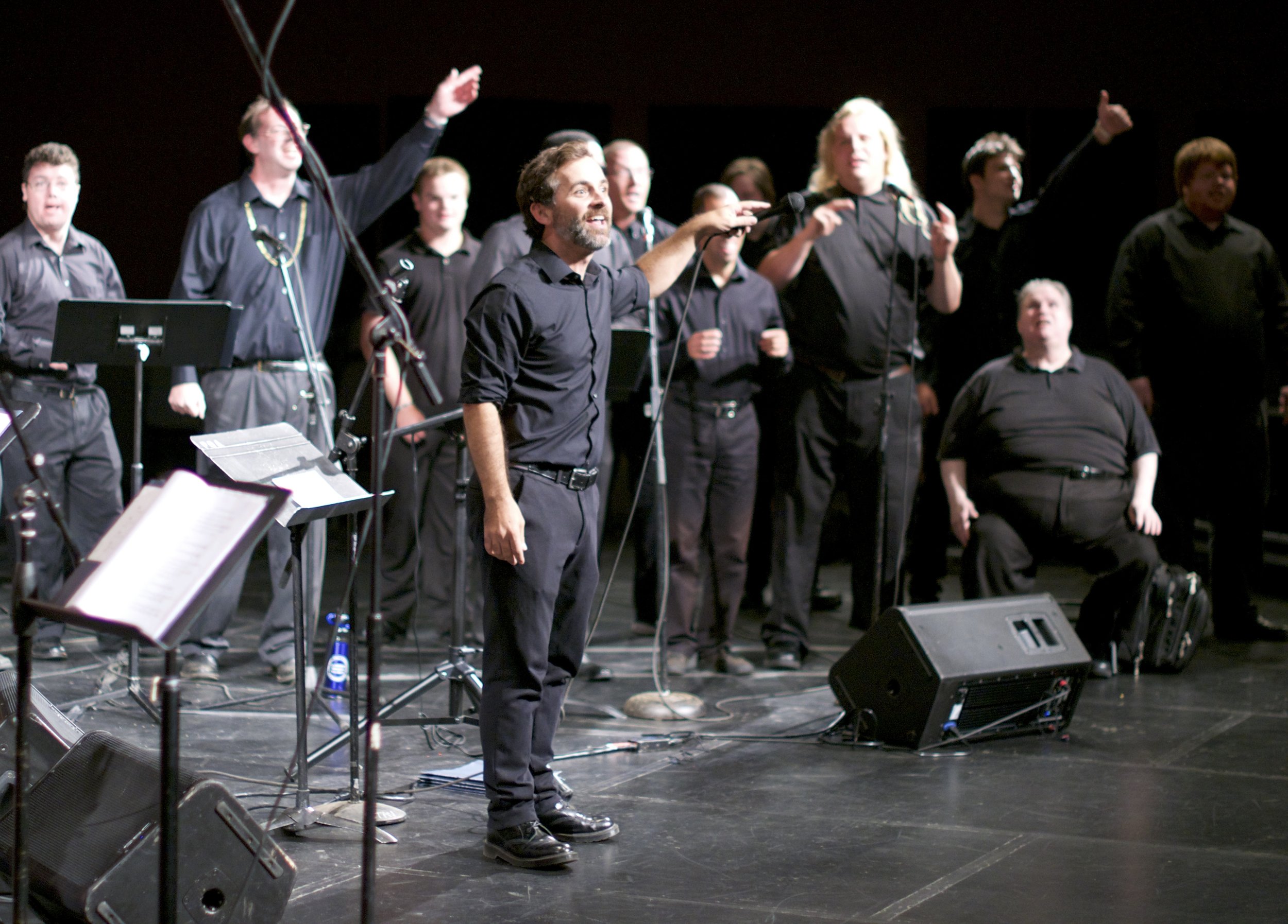 Large group of people stands in a black box theatre in front of sound equipment