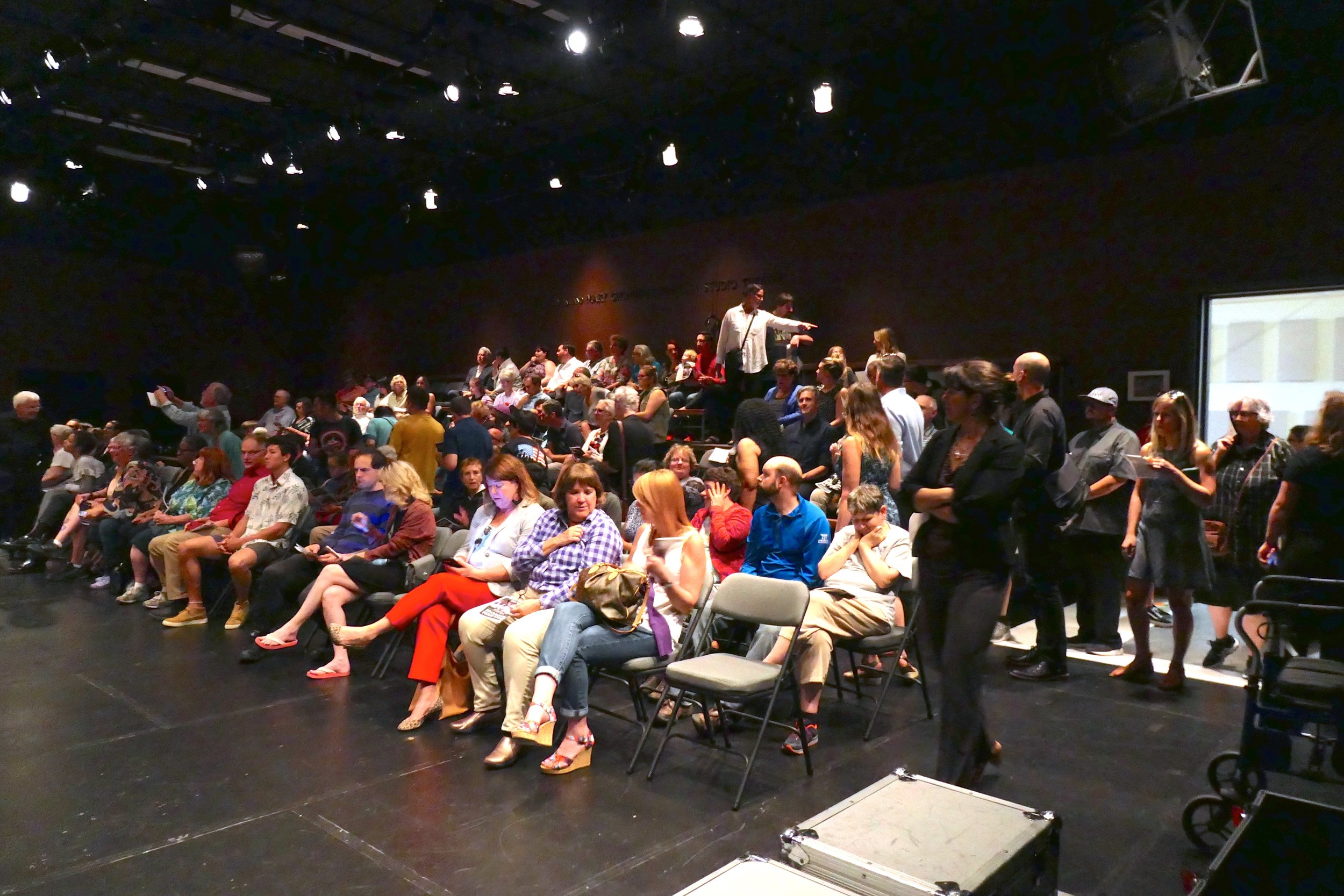 Full audience of seated people in a black box theatre