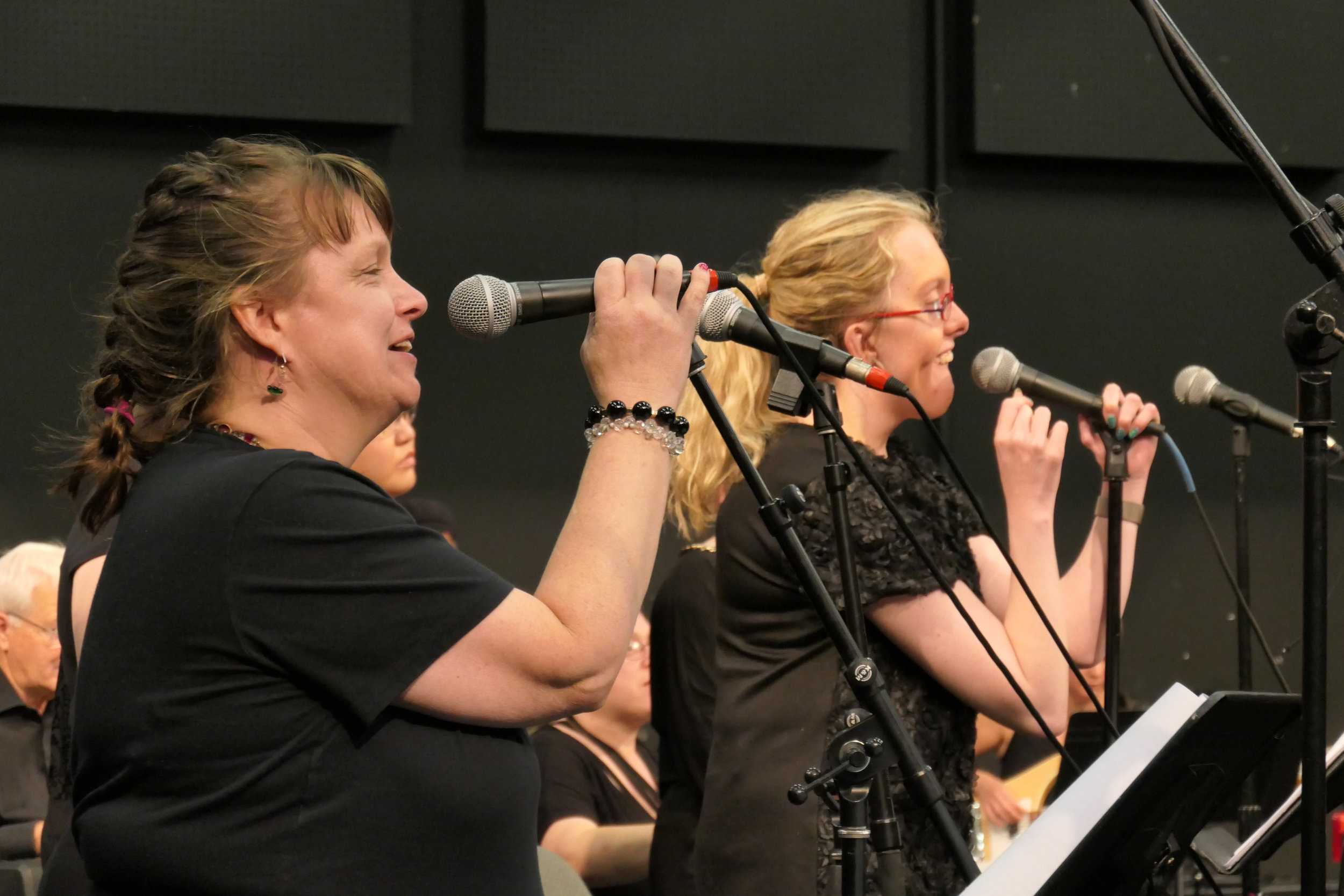 Two women wearing black seen from the side, holding microphones